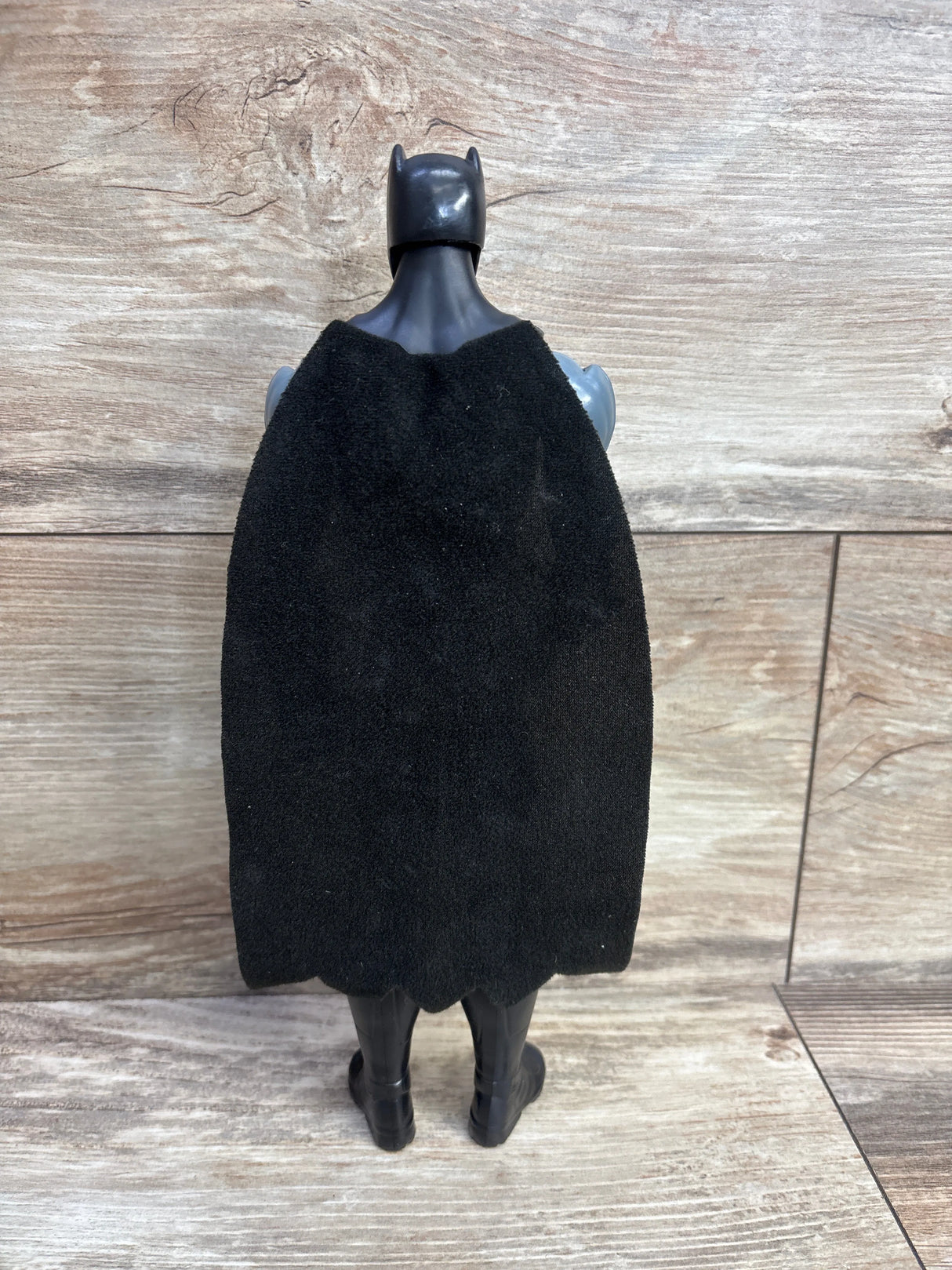 Back view of a black Batman action figure with a fabric cape standing on a wooden surface