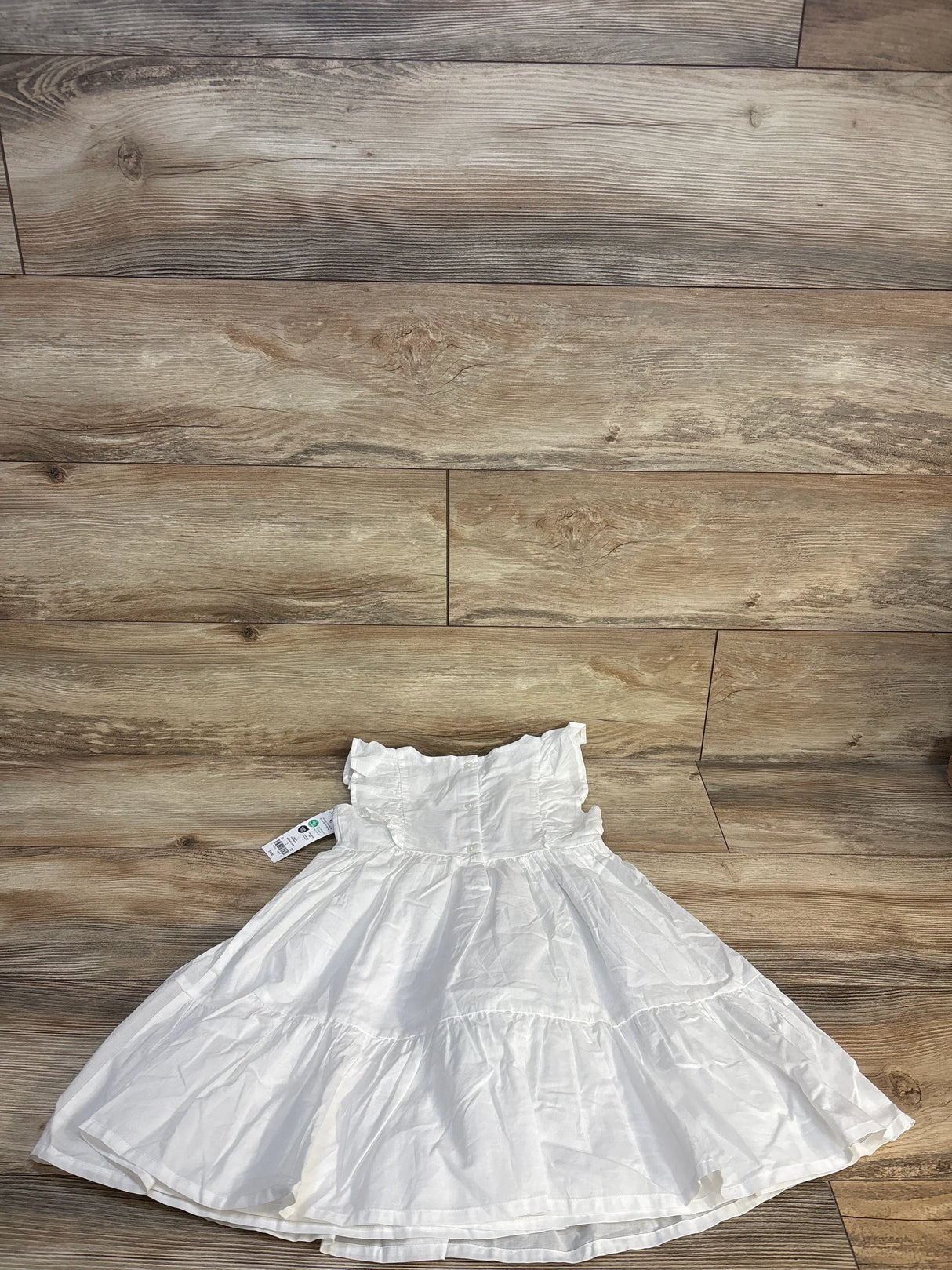 White ruffled girls dress with tag, displayed on wood floor, children's clothing