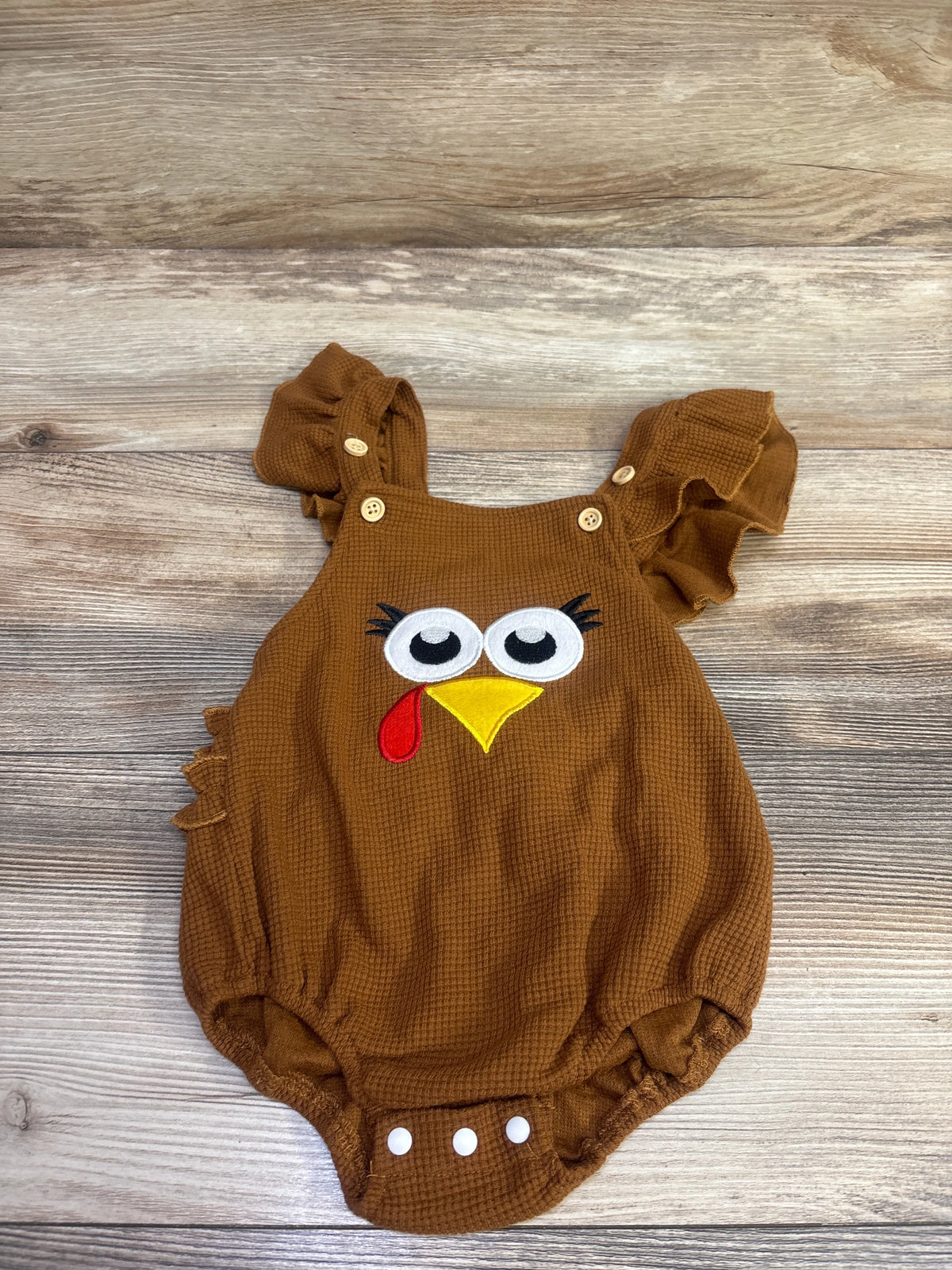 Front view of brown Thanksgiving bubble romper showcasing ruffled sleeves and turkey face appliqué on a wood-grain background