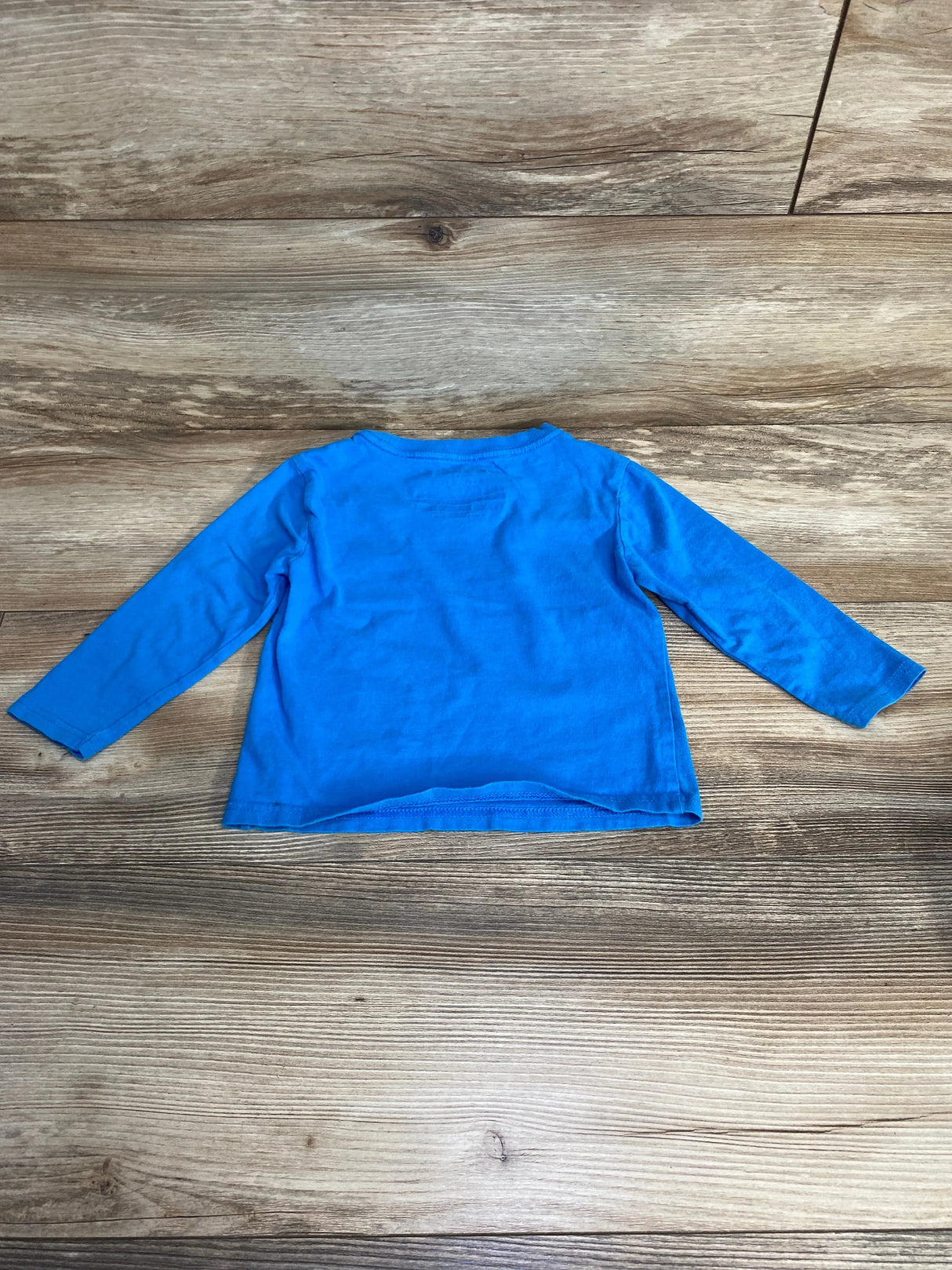 Flat-lay of Nautica toddler long-sleeve shirt, bright blue, size 2T, showing crew neck and straight hem on wood background