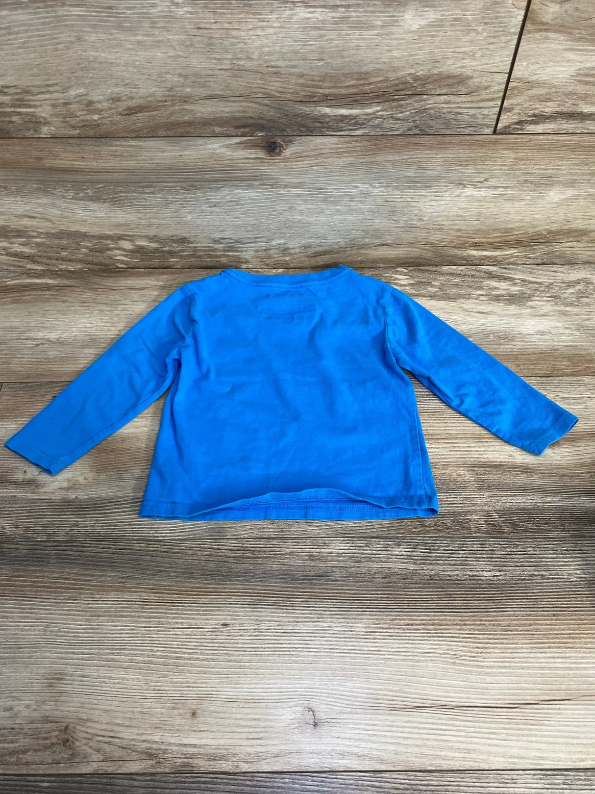 Flat-lay of Nautica toddler long-sleeve shirt, bright blue, size 2T, showing crew neck and straight hem on wood background