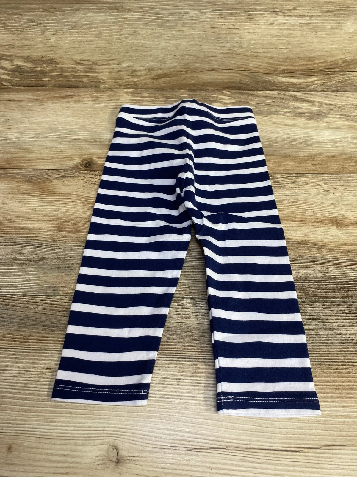 Flat lay of navy and white zebra-striped toddler leggings size 3T showing full-length horizontal stripes on wood background