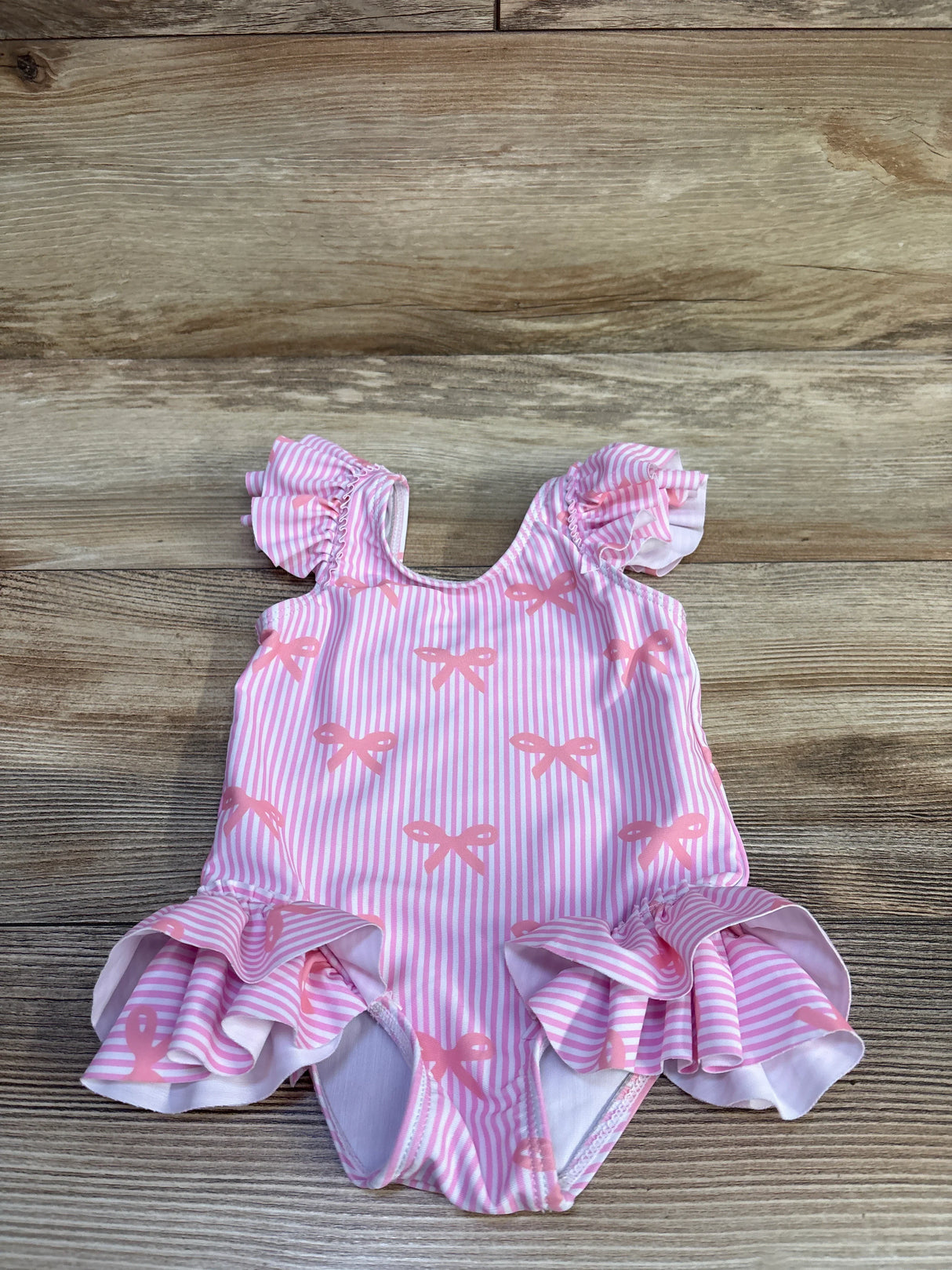 Front view of pink striped baby one-piece swimsuit with bow print, ruffled sleeves and skirt on wood background