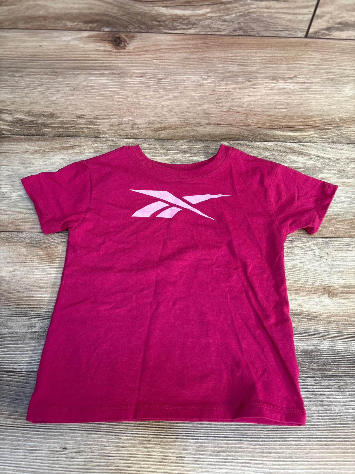 Pink kids Reebok t-shirt with white logo, laid on wood floor for resale