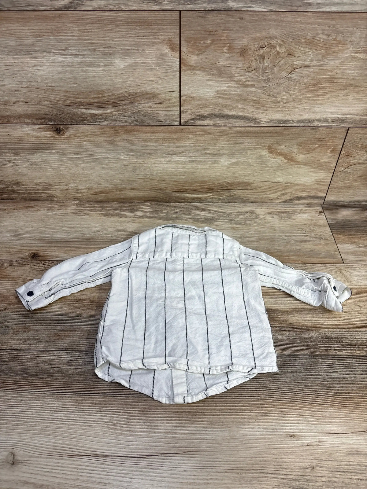 White long-sleeve toddler shirt with black vertical stripes on wooden floor
