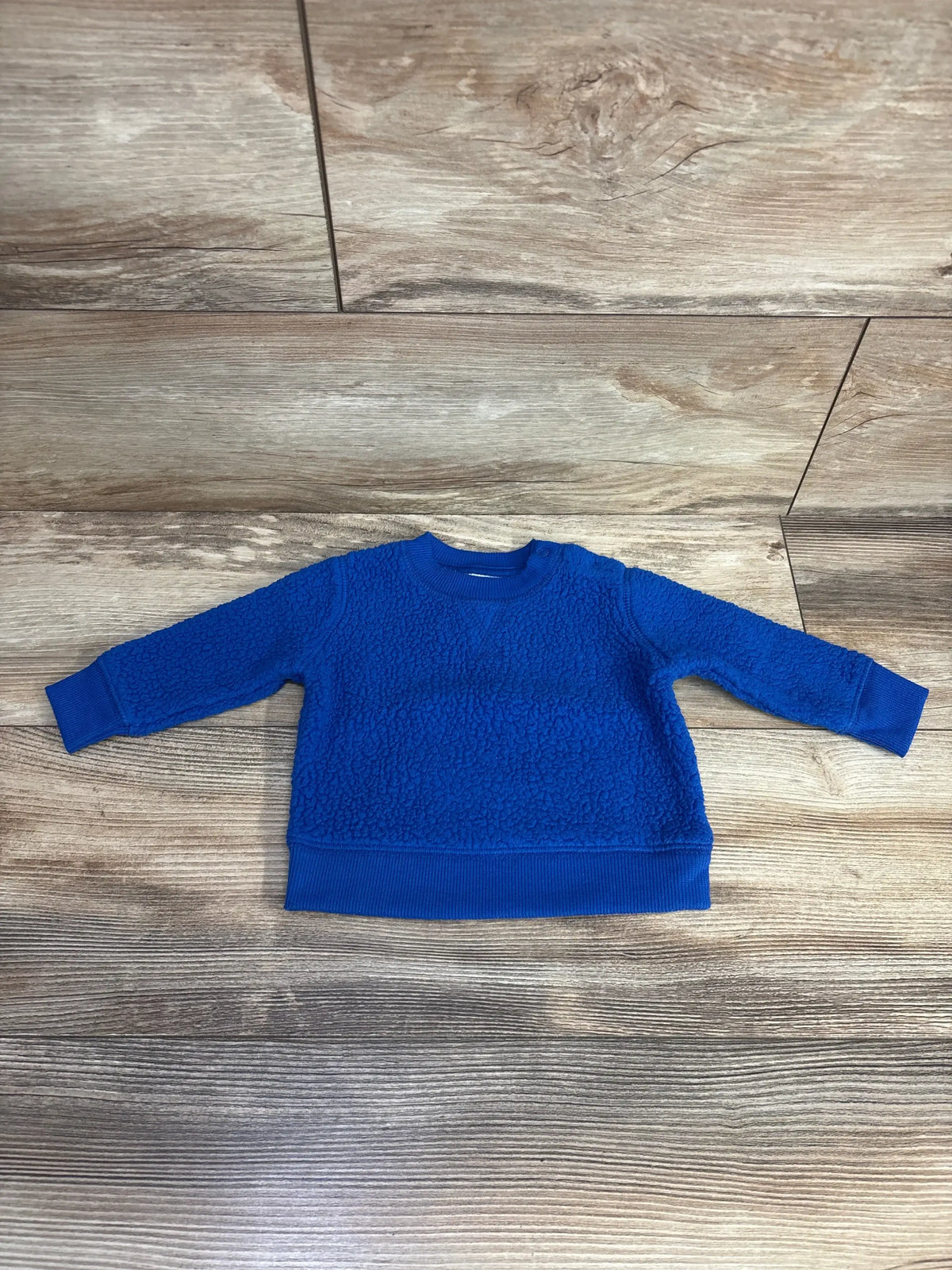 Flat lay of Cat & Jack sherpa pullover sweater, blue, size 0-3M, showing soft textured fleece and ribbed cuffs on wood floor