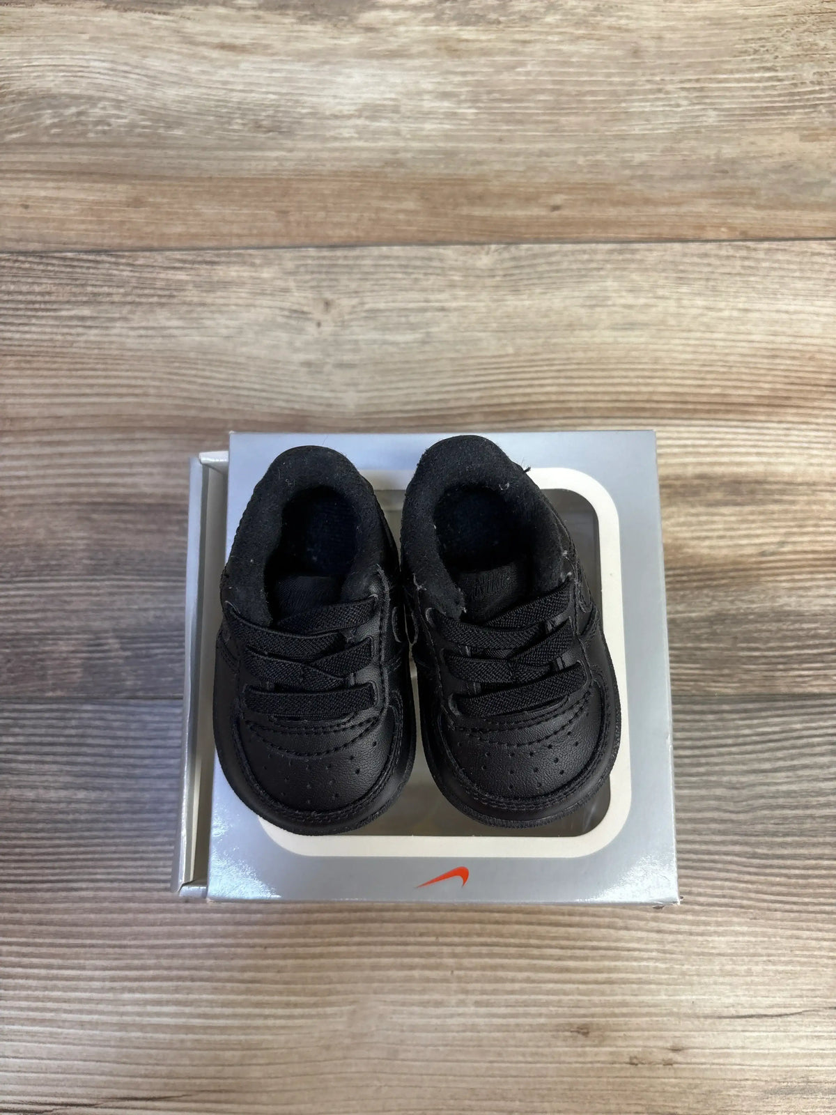 Top view of Nike Air Force 1 crib shoes in black, size 1C, showcasing lace closure and padded collars on a Nike shoebox