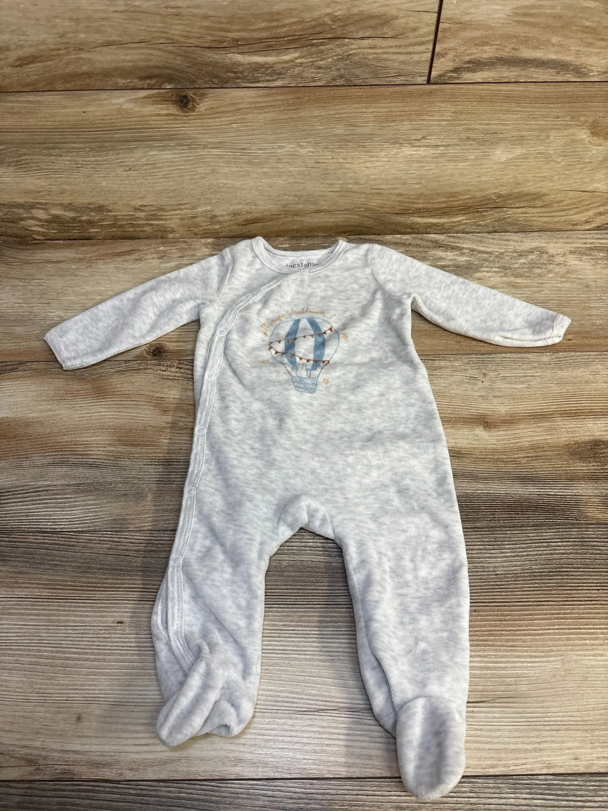 Light gray baby onesie with blue hot air balloon design laid on wooden floor