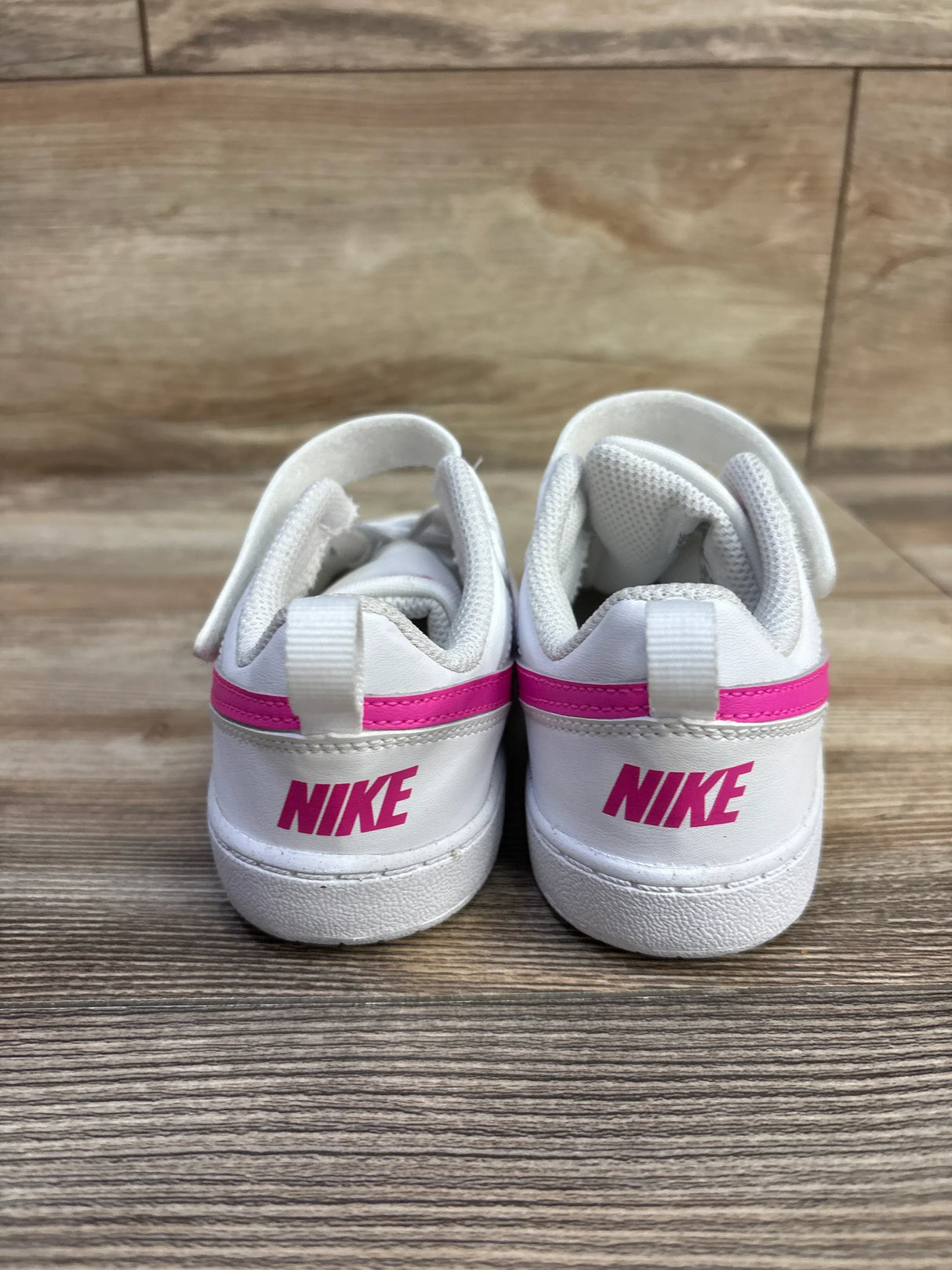 Rear view of Nike Court Borough Low Recraft toddler sneakers showcasing white leather, pink heel stripe and pink NIKE logo on wood floor