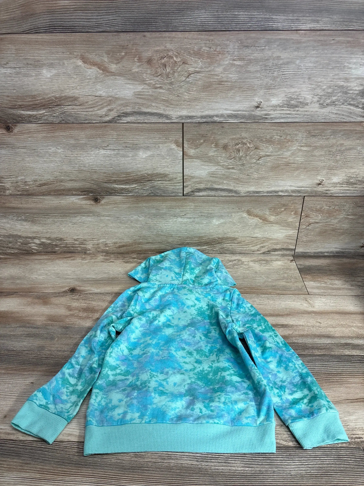 Back view of teal tie-dye My Little Pony Rainbow Dash hoodie showing hood and ribbed cuffs on wood background