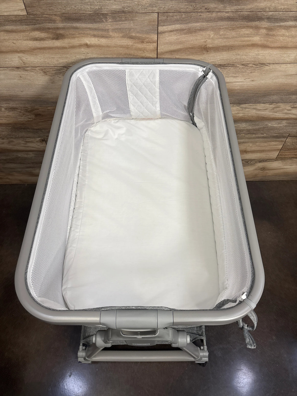 Mesh-sided portable baby bassinet with white mattress on wood floor
