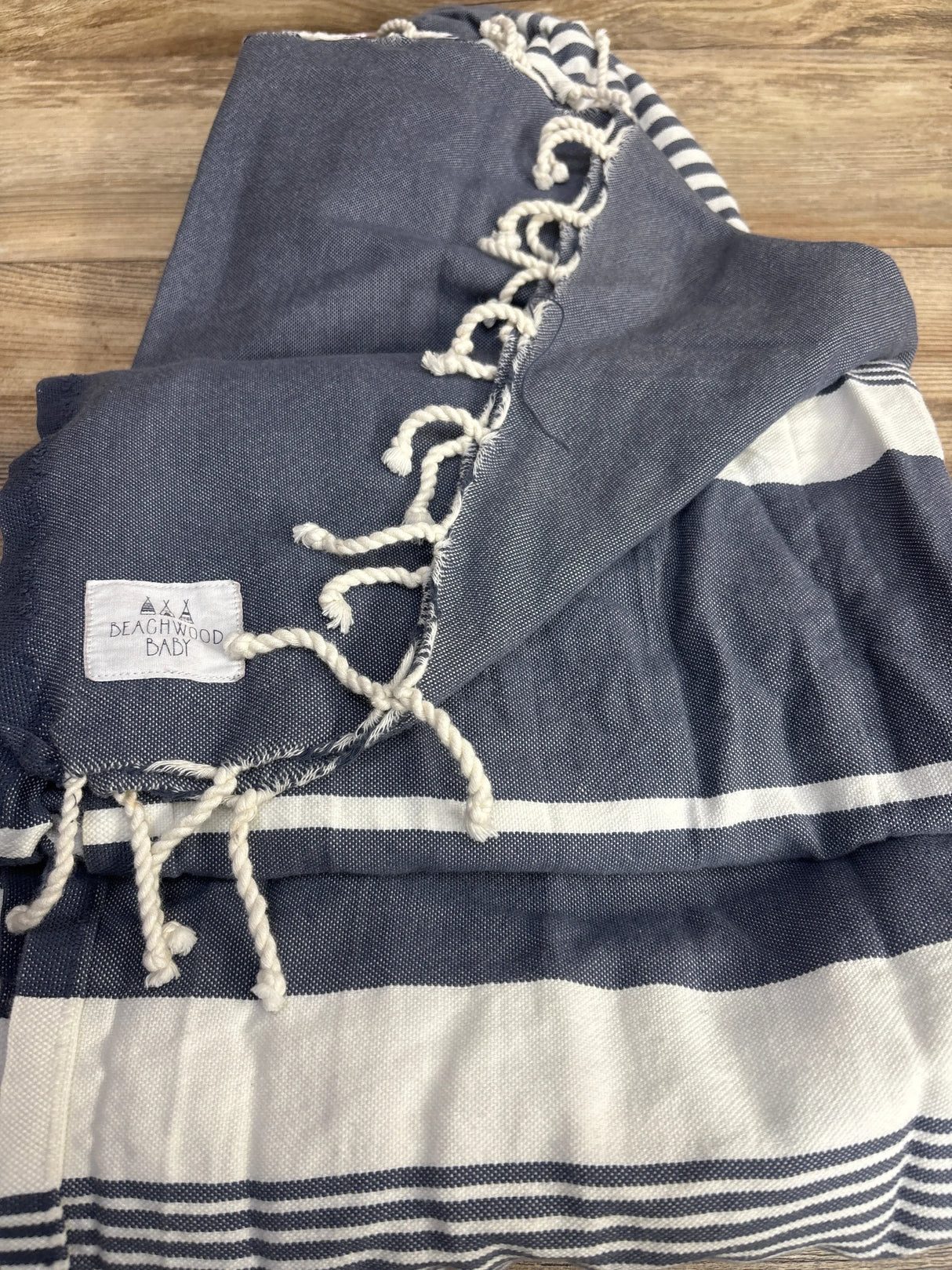 Folded handwoven navy and white ring sling showcasing horizontal stripes and twisted tassels on a wood surface