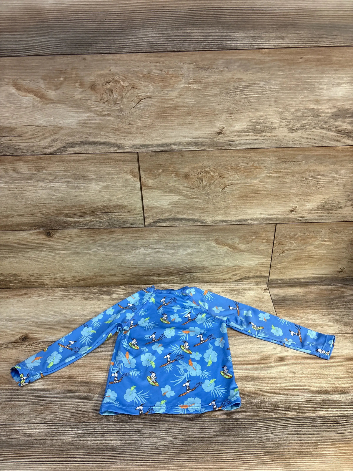Flat lay of Zara x Peanuts blue long-sleeve quarter-zip rash guard top showing allover character print on wood-look floor