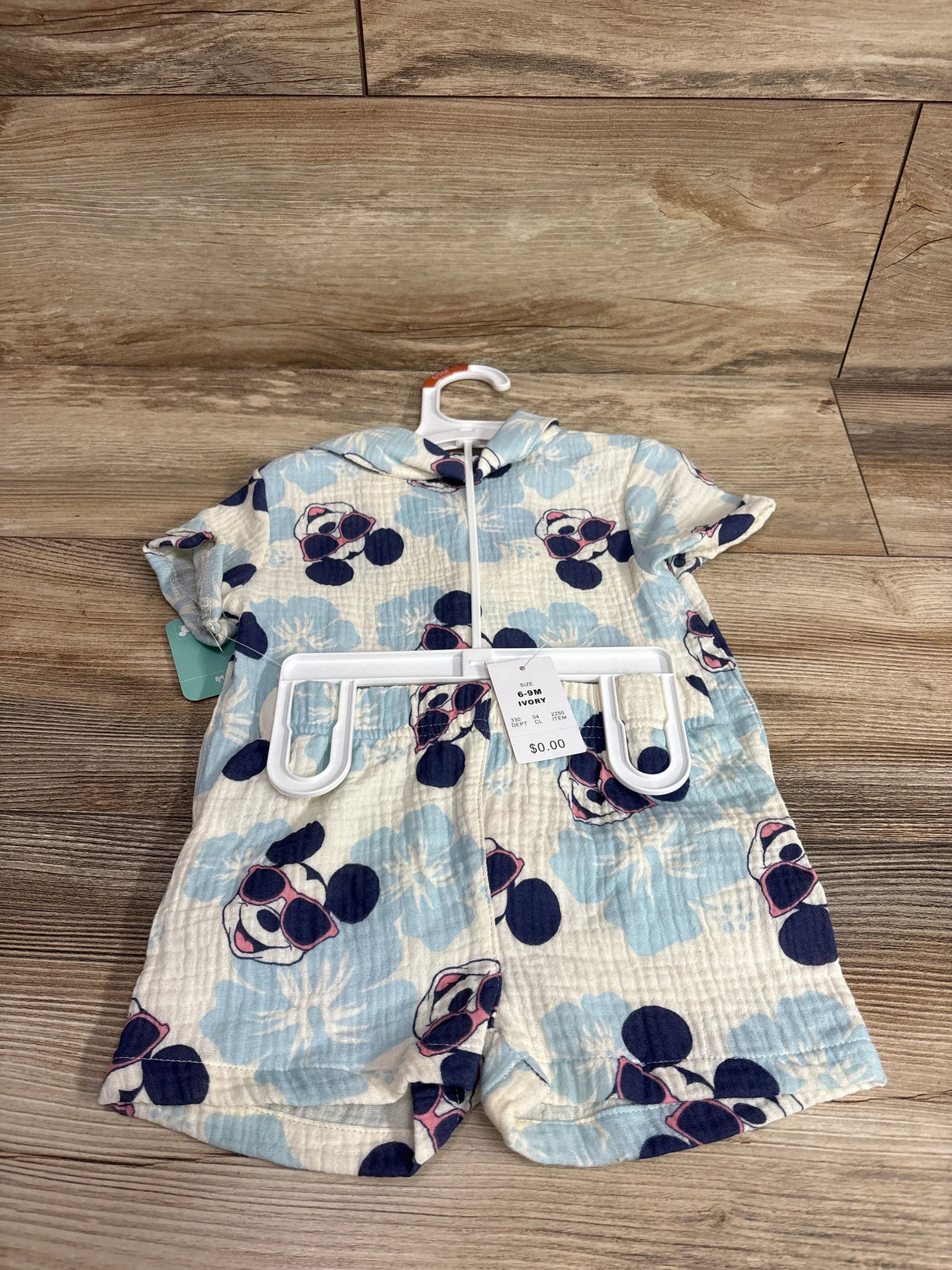 Front flat-lay of ivory gauze button-up baby top and shorts with blue floral and Mickey print, size 6-9M tag on wood floor