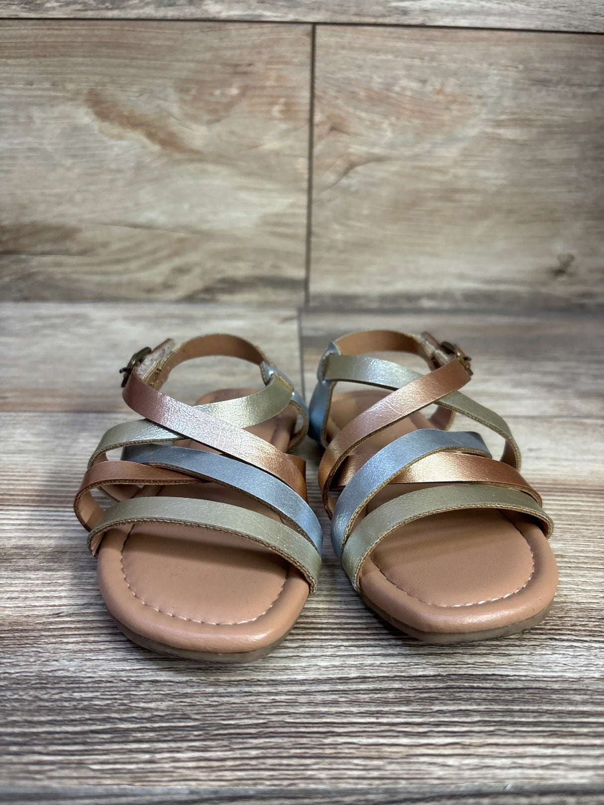 Front view of Old Navy metallic faux leather toddler sandals with multicolor crisscross straps and ankle buckle on wood floor