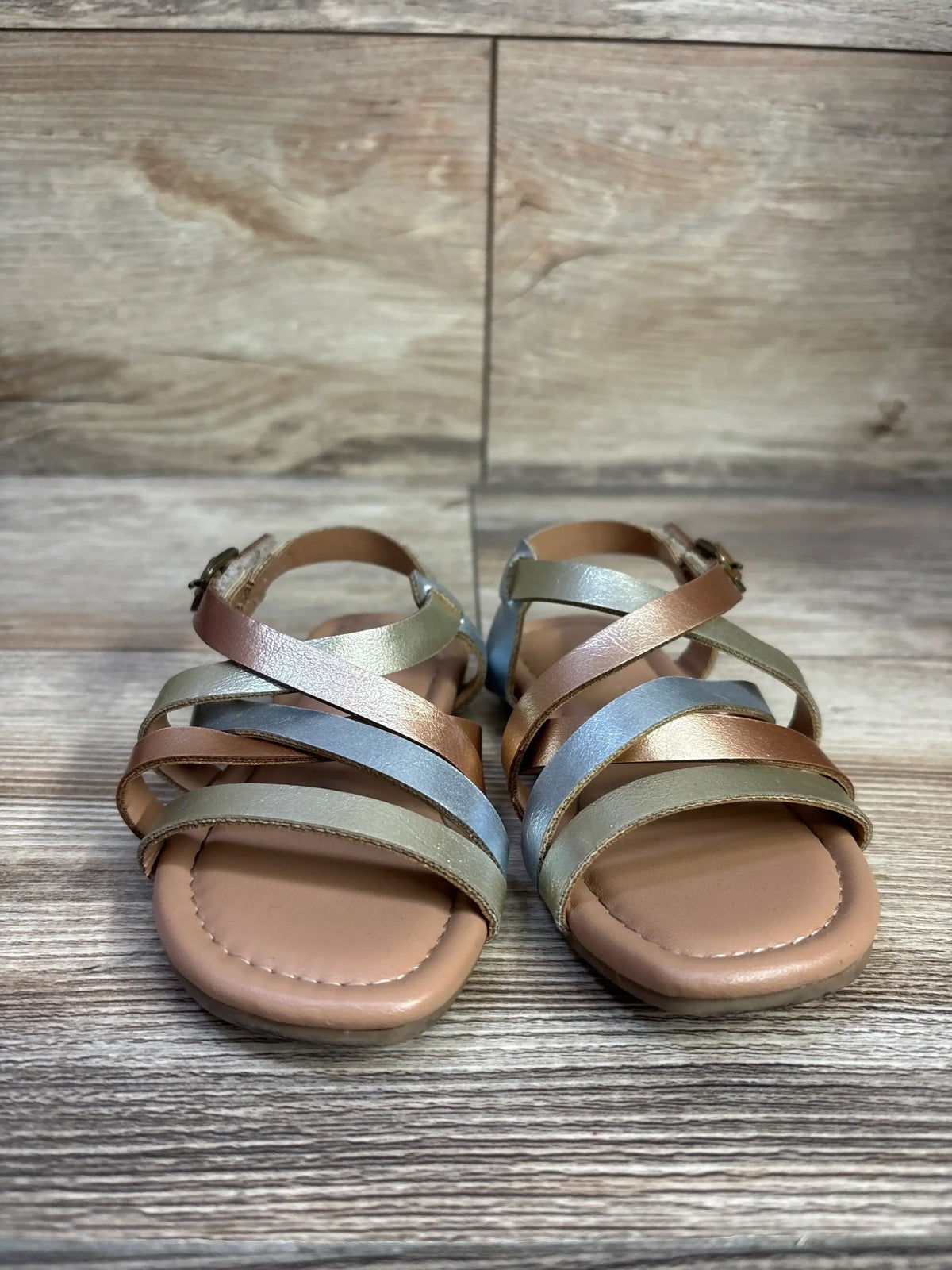 Front view of Old Navy metallic faux leather toddler sandals with multicolor crisscross straps and ankle buckle on wood floor