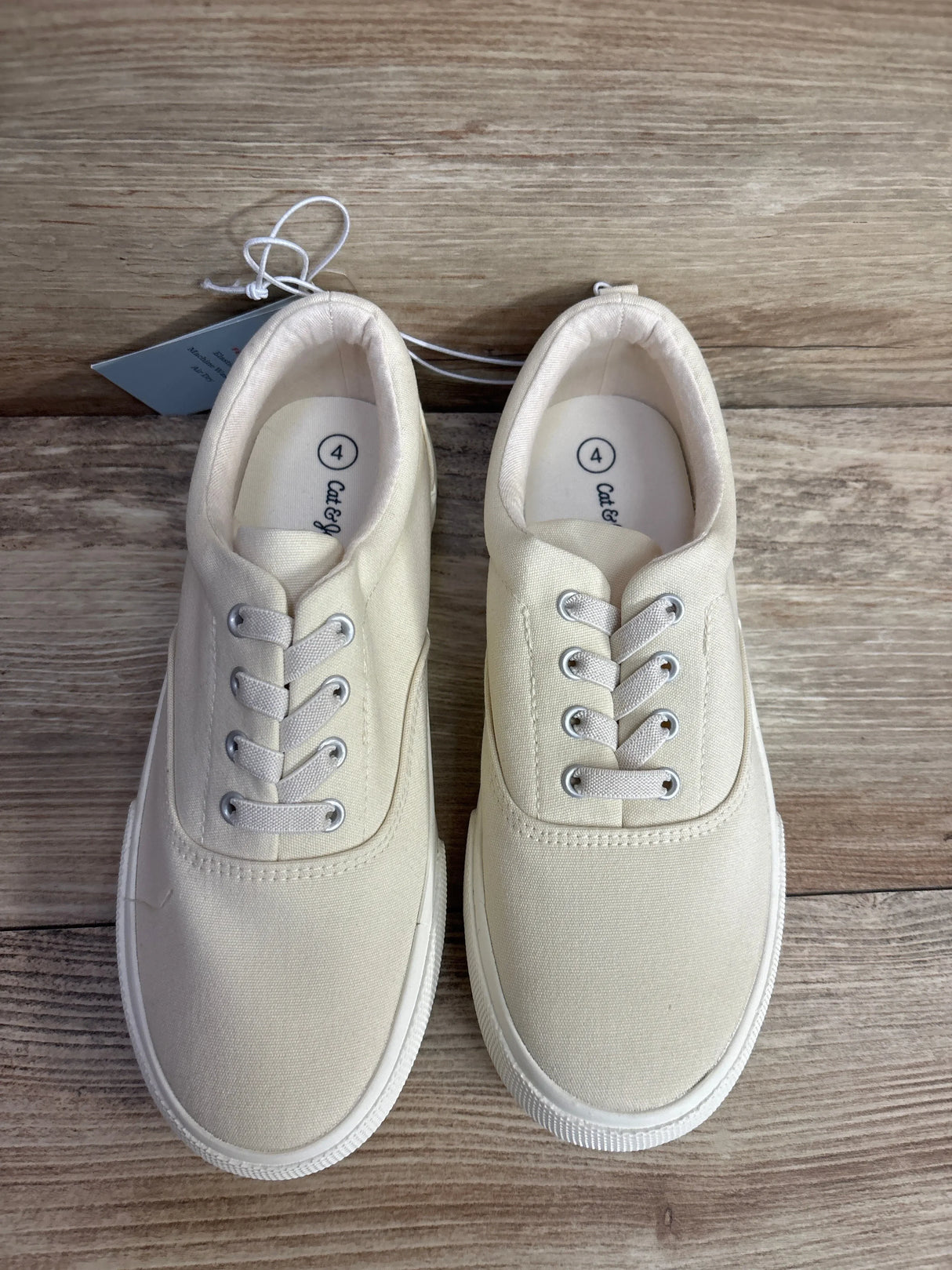Pair of ivory canvas toddler sneakers with laces on a wooden floor, size 4.