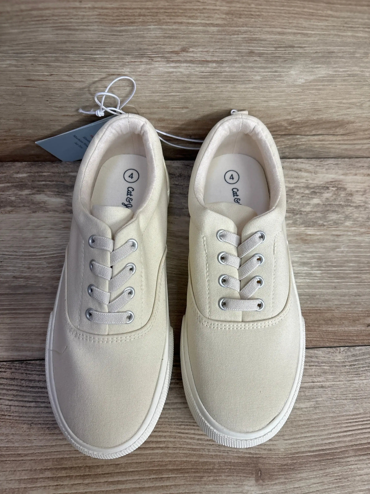 Pair of ivory canvas toddler sneakers with laces on a wooden floor, size 4.