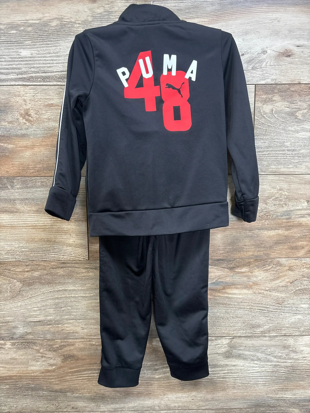 Kids black PUMA tracksuit with red 48 graphic on back, laid flat on wooden floor