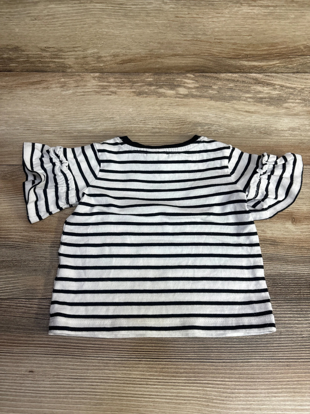 Children's black and white striped short-sleeve shirt with ruffled sleeves on wood background