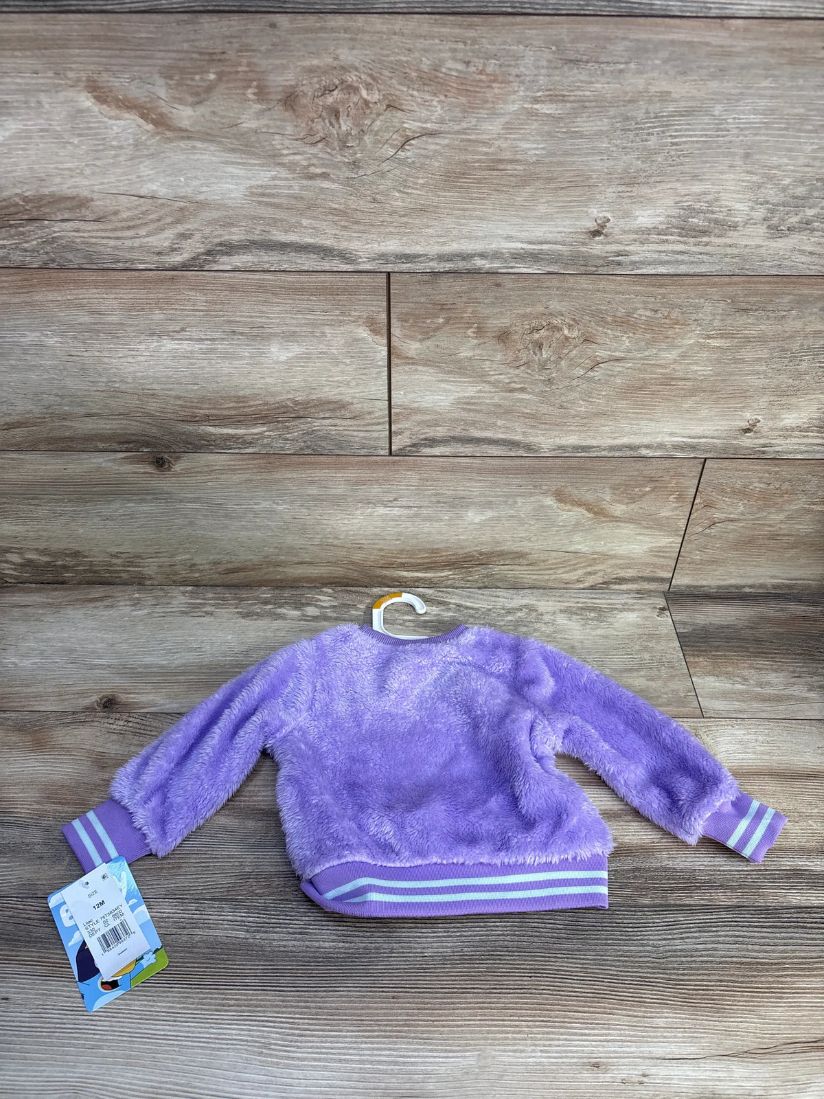 Front view of Bluey purple plush sweatshirt showcasing striped cuffs and hem on a wood-grain background
