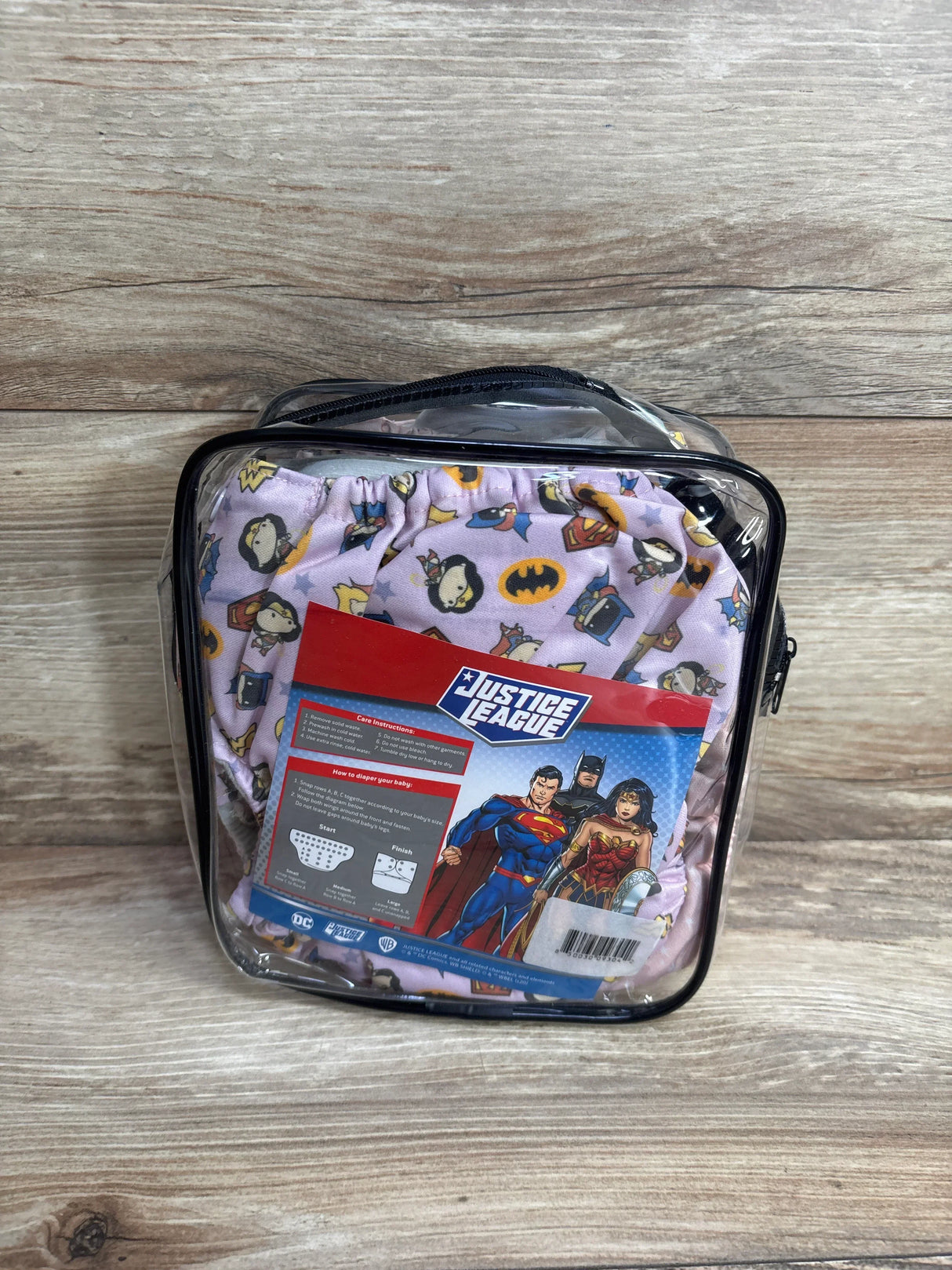 Justice League themed reusable cloth diaper set in clear zippered pouch on wood background