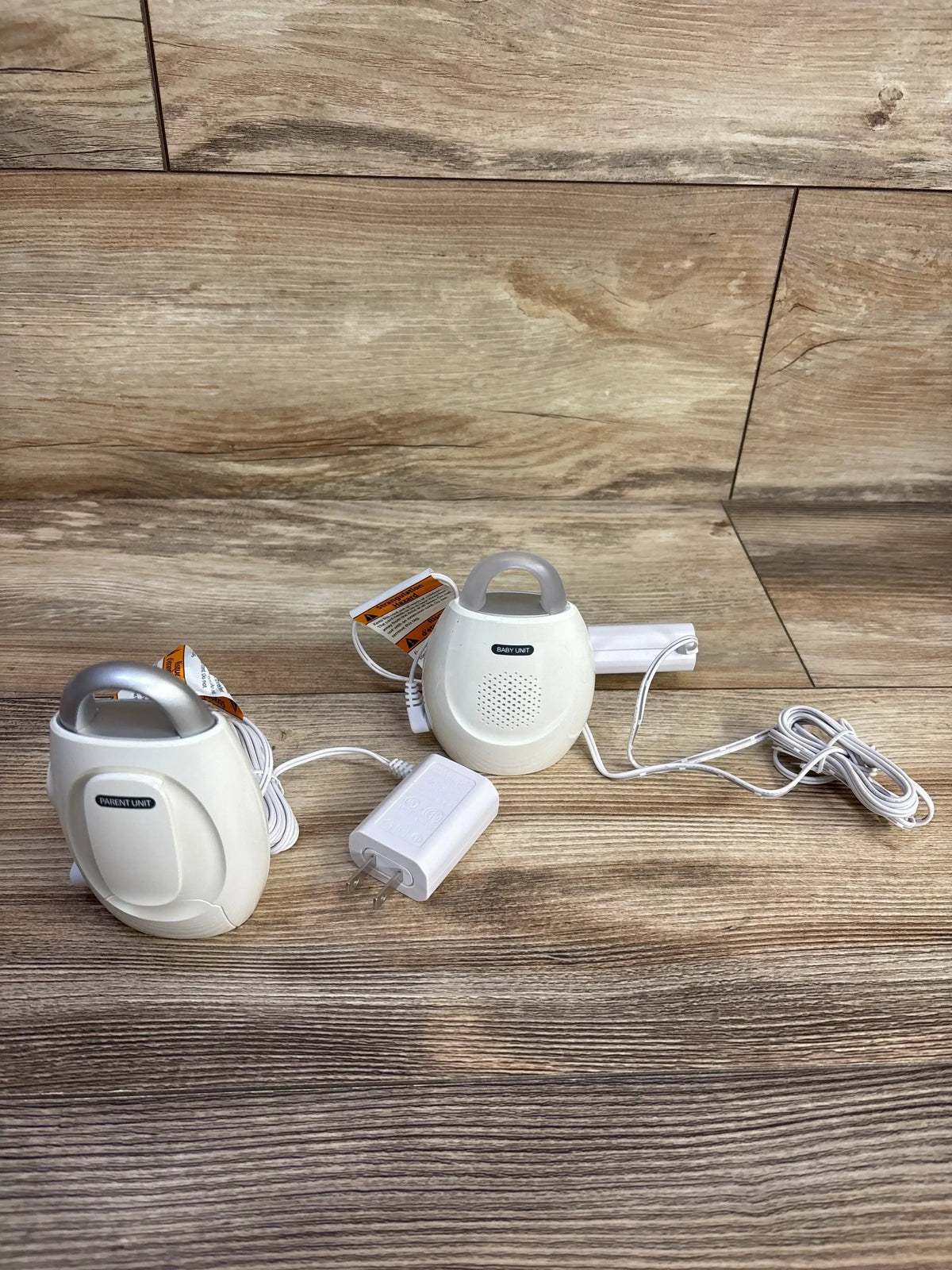 Flat lay of VTech DM221 audio baby monitor showcasing two white parent and nursery units with power cords on wood plank background