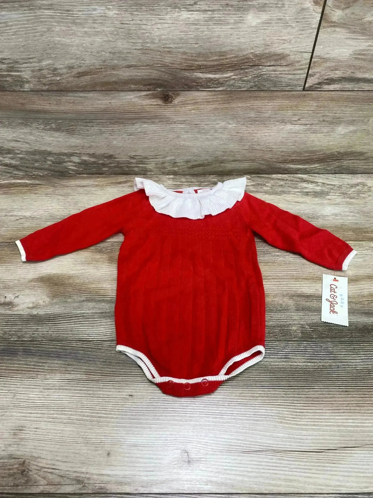 Front view of a red Cat & Jack romper showcasing a white ruffle collar and trim on a wood-grain background