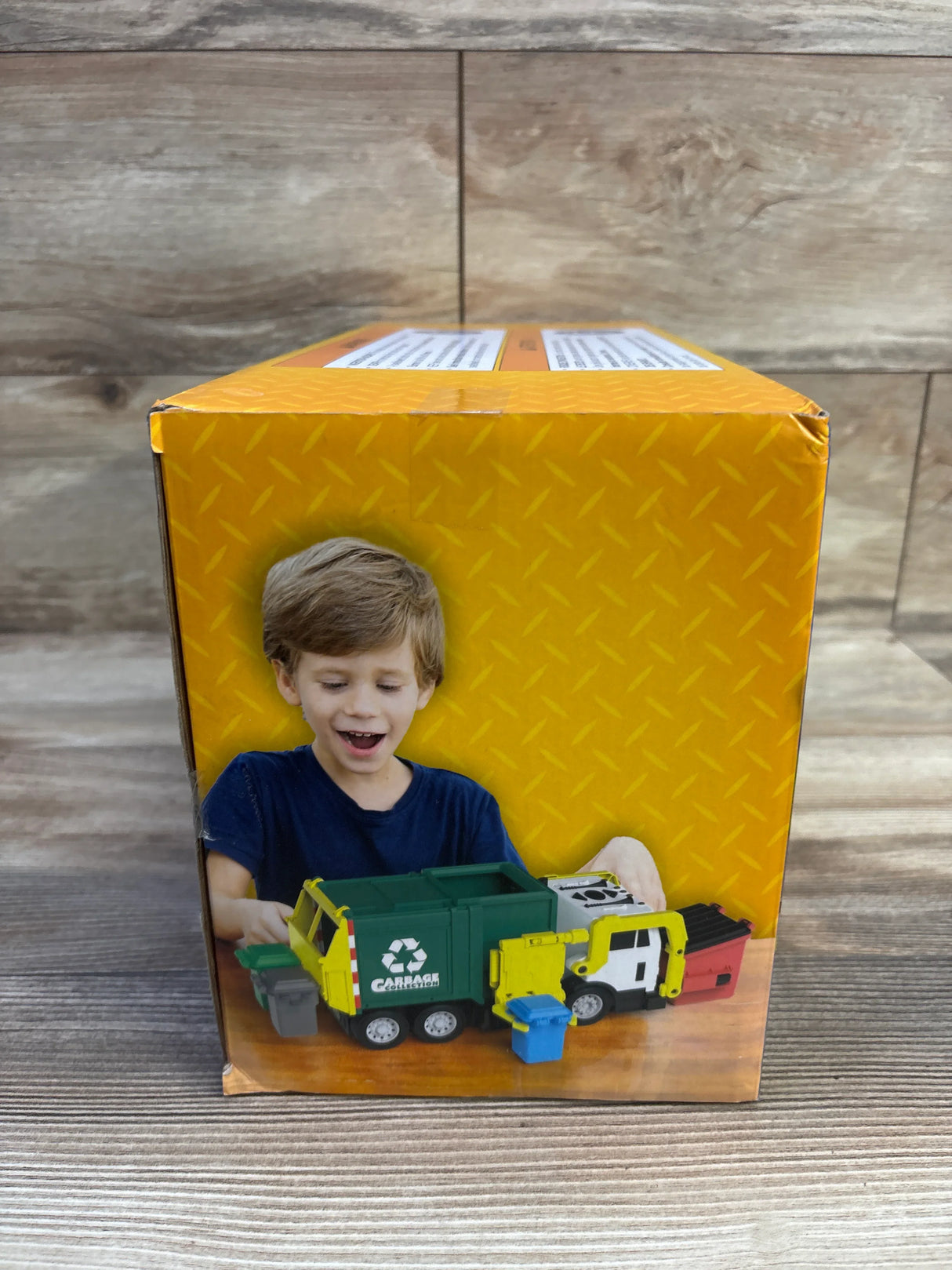 Box front showing Joyfy Play-Act 16 inch garbage truck toy with a child playing with the green and yellow truck on a yellow background