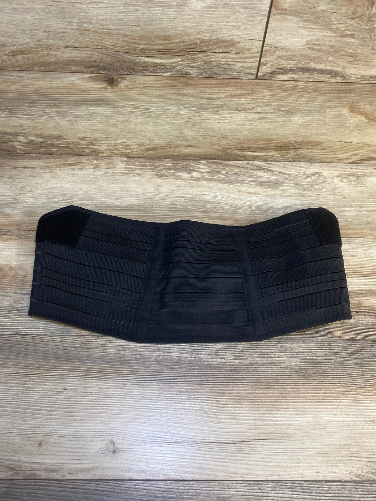 Black elastic maternity support belt on wood floor, postpartum belly band