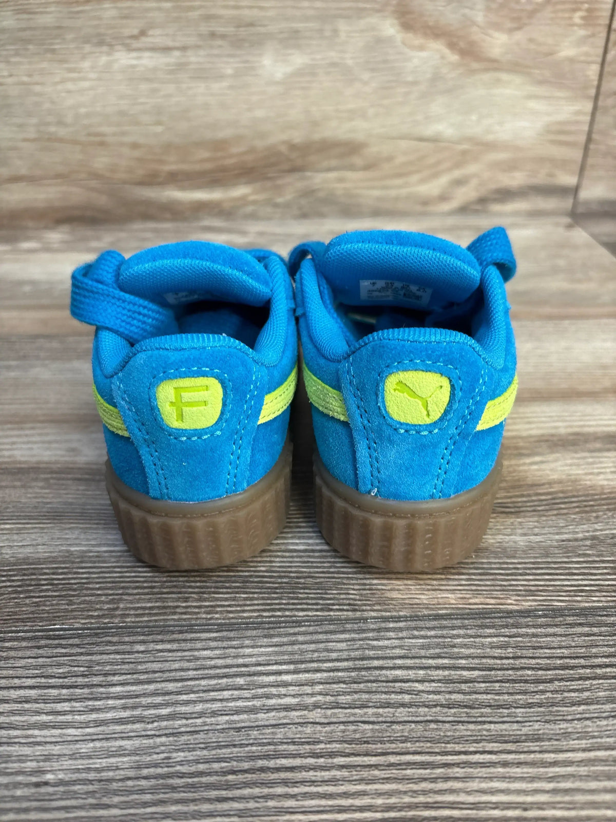 Back view of Puma x Fenty Creeper Phatty Sneakers sz 8c NWT showcasing blue suede upper with yellow Puma logo and gum sole on wood plank floor