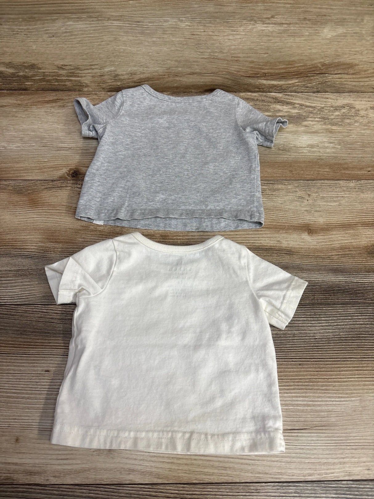 Two short sleeve toddler t-shirts, one grey and one white, laid flat on wood background