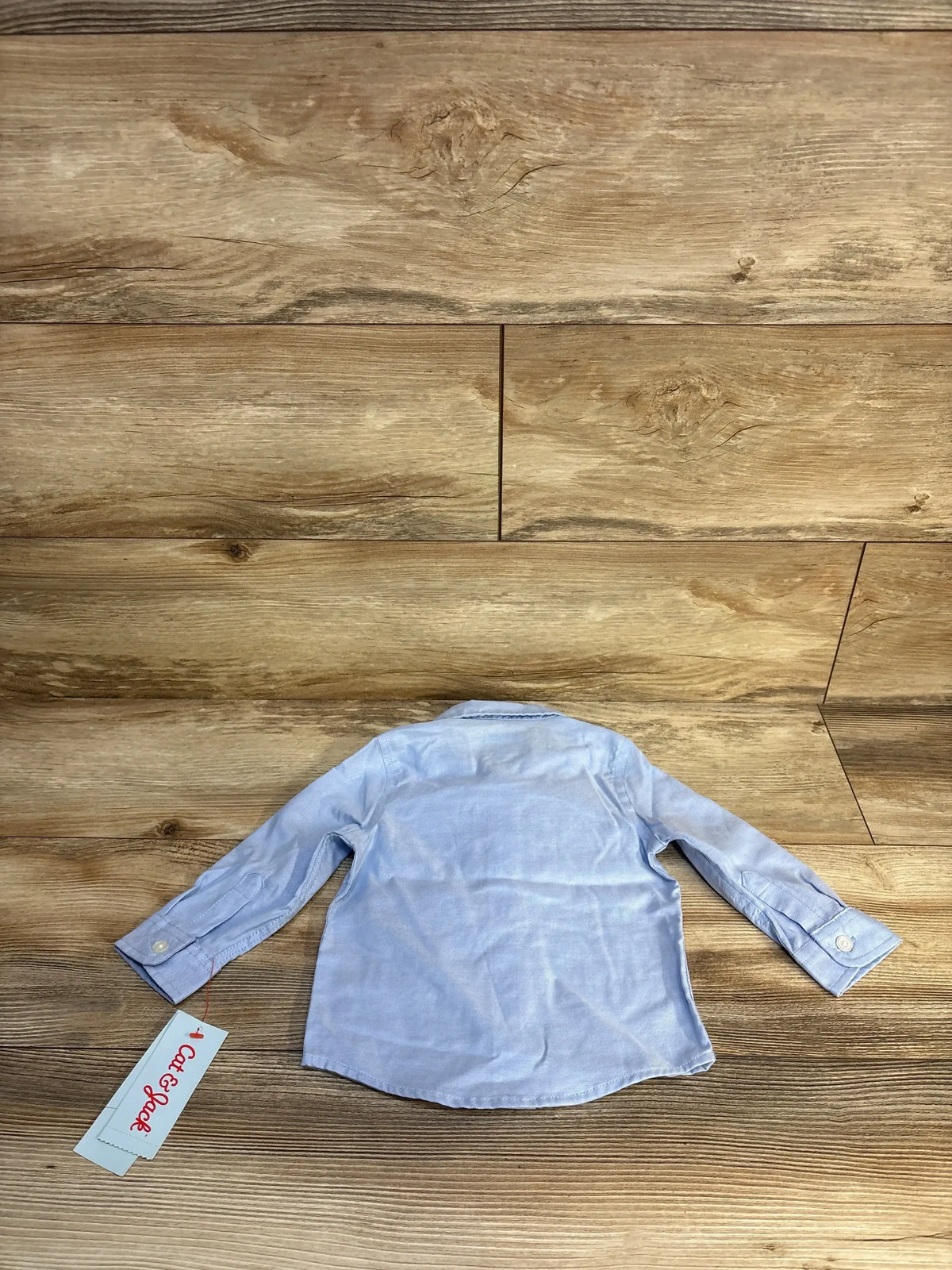 Light blue long sleeve baby shirt displayed on wood background with a tag attached
