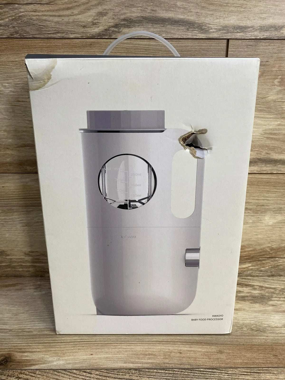 Front of NEW KWASYO Baby Food Maker white box showcasing pitcher style processor with measurement window on wood plank floor