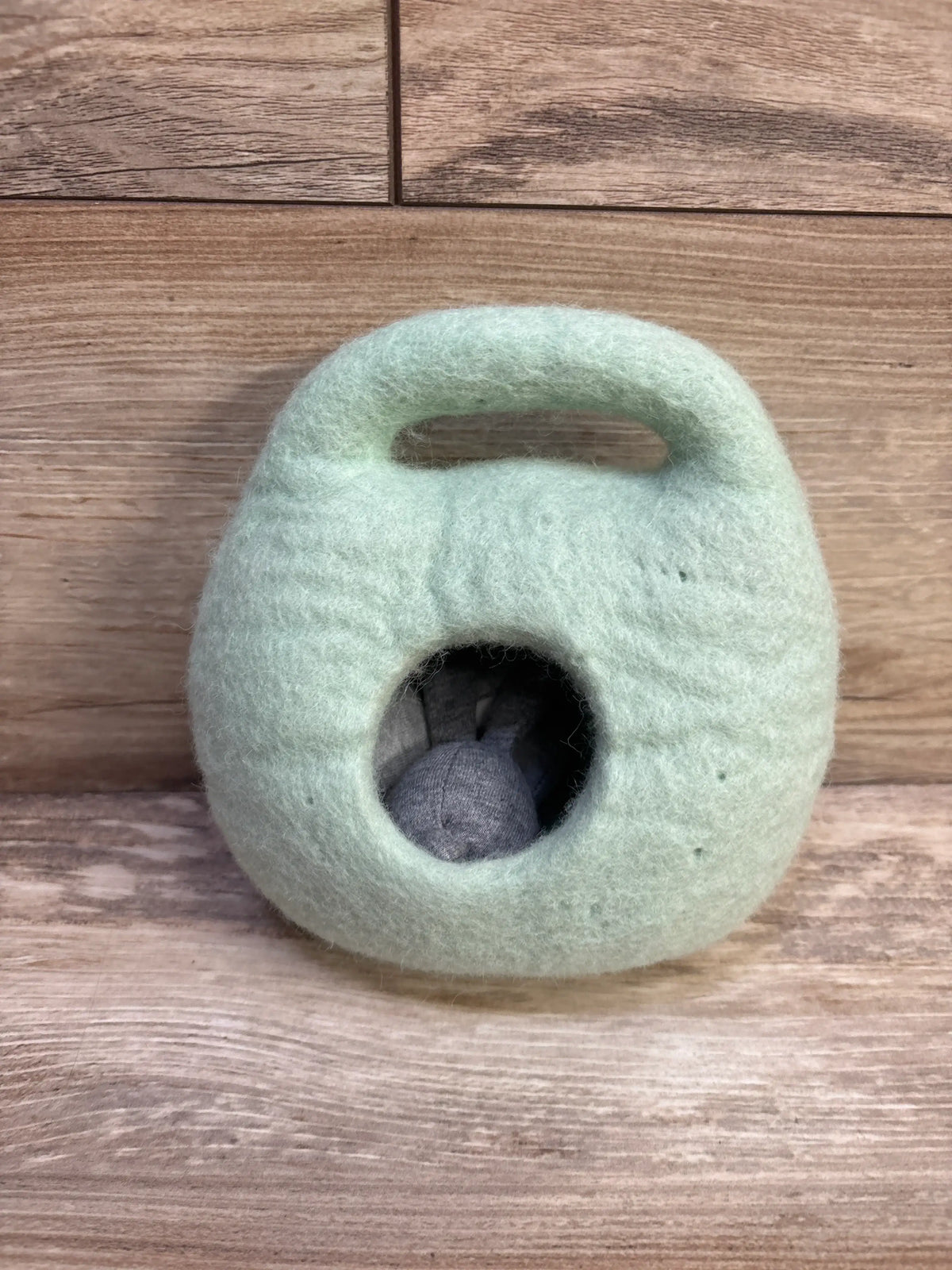 Front view of Lovevery Bunnies In A Felt Burrow Playset showcasing a bunny inside its pale green felt burrow on a wood-grain surface