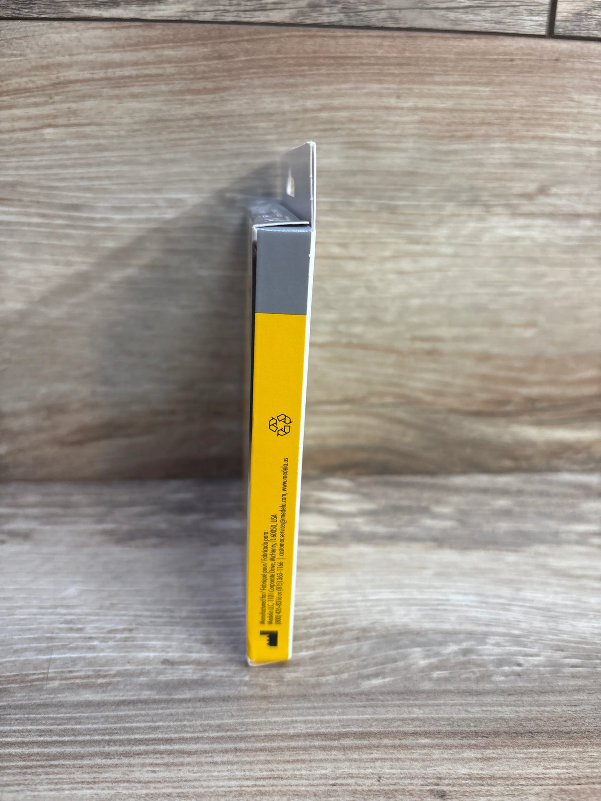 Side view of a yellow and gray product box with recycling symbol on wooden surface