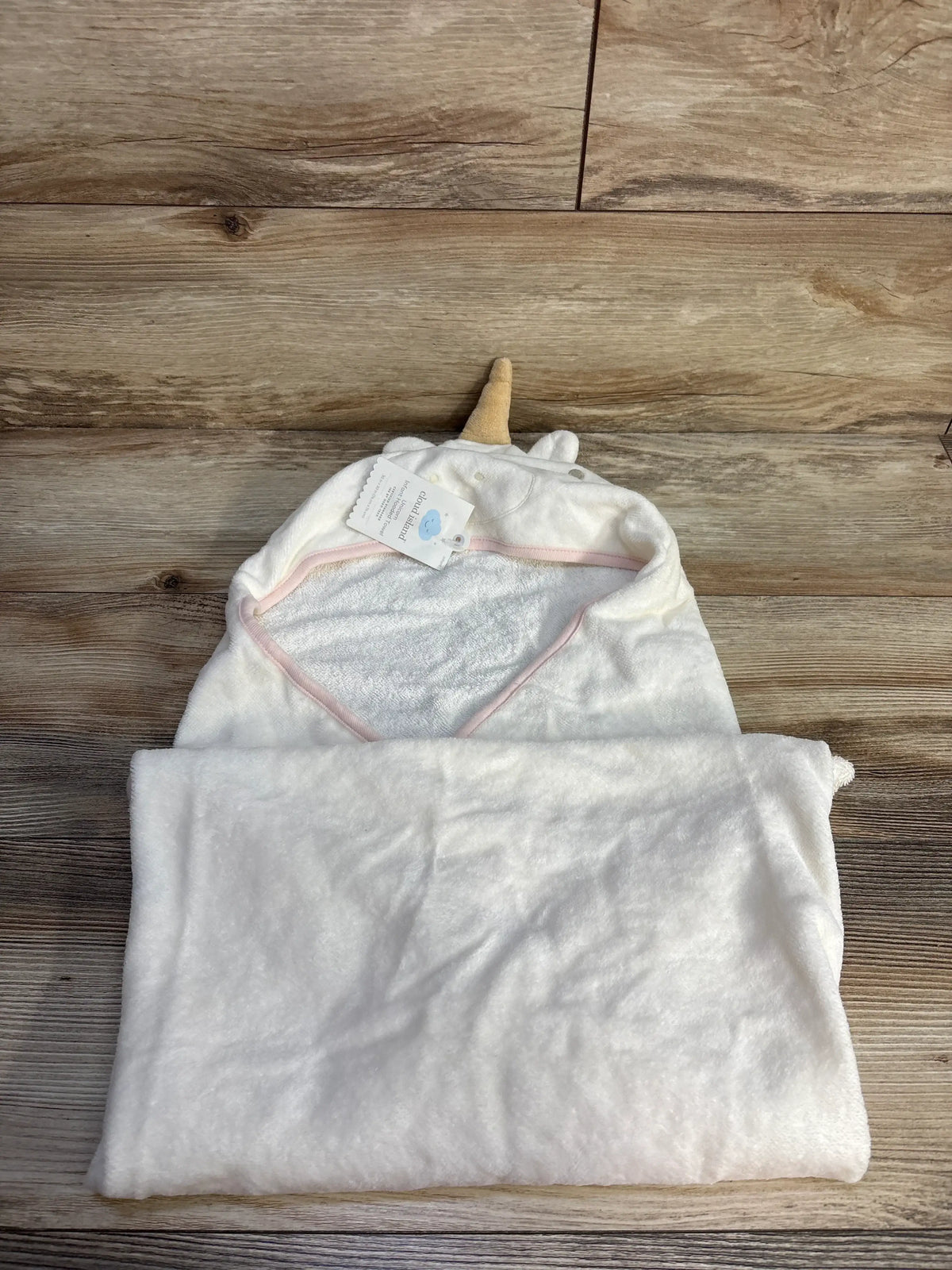 Top-down view of a cream Cloud Island unicorn hooded towel showcasing its horn, hood, and pink trim on a wood surface