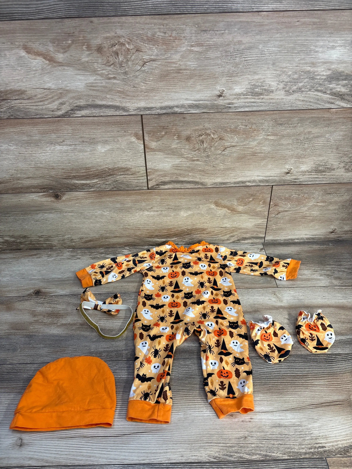 Top view of Kucnuzki 4pc Halloween coverall set showcasing orange Halloween print with matching mittens, hat, and headband on a wood floor