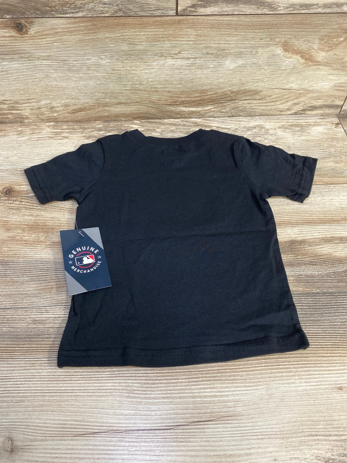 Back view of black Colorado Rockies toddler T-shirt showcasing blank back and attached Genuine Merchandise MLB hang tag on a light wood background