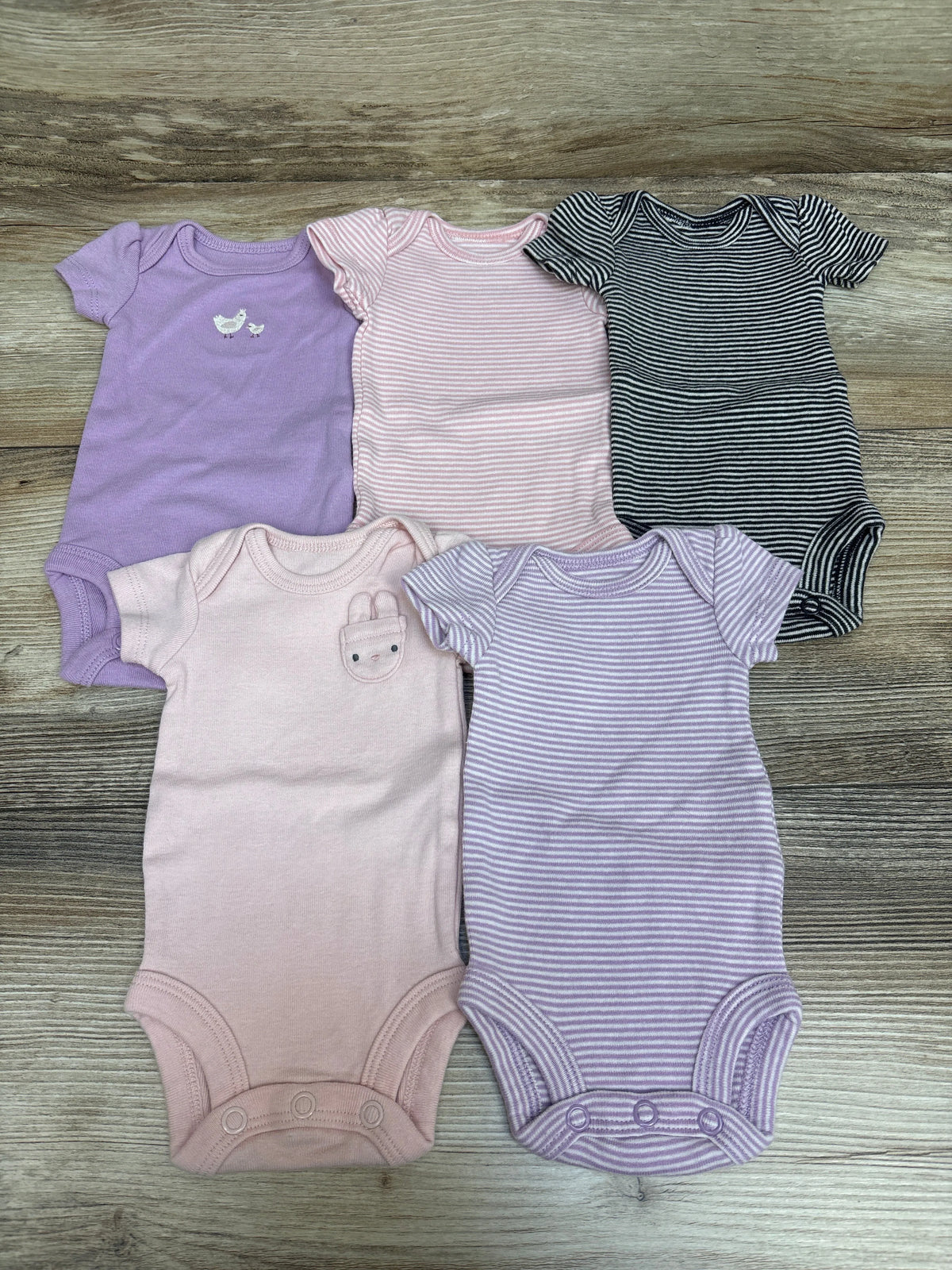 Top-down view of Carter’s five preemie bodysuits showcasing purple, pink, and striped designs on a wood surface