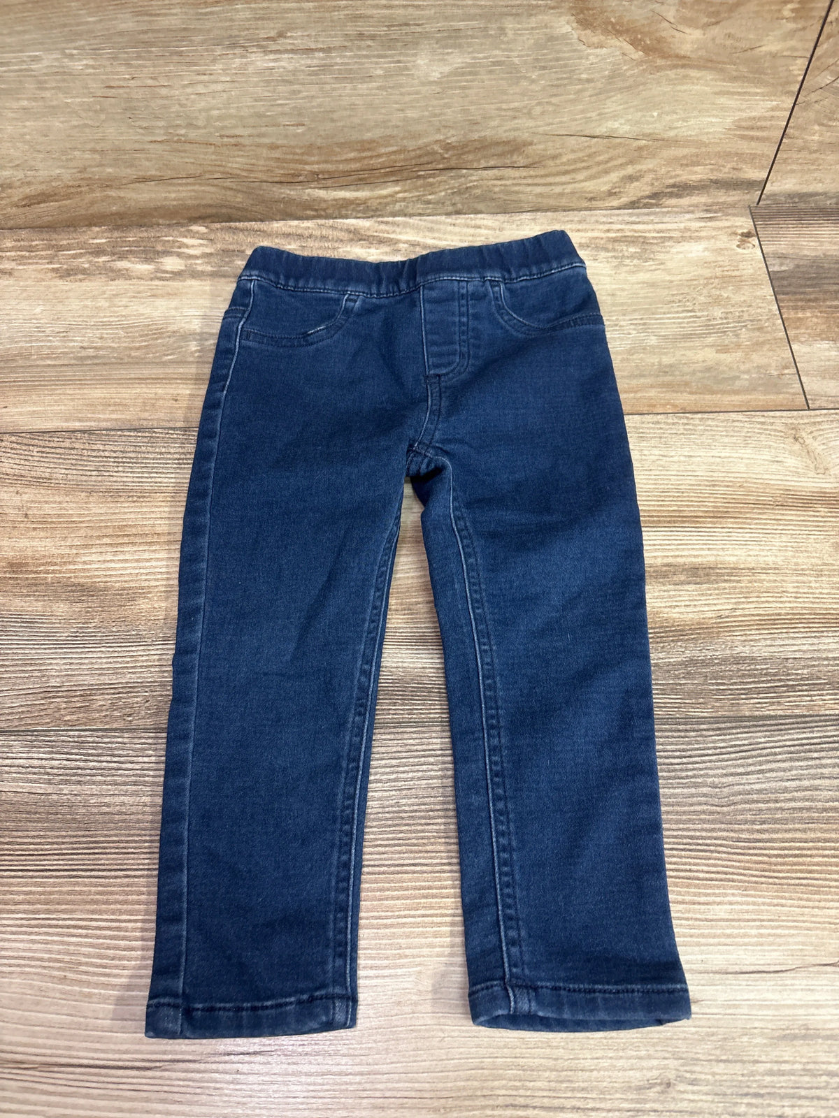 Front view of blue Pekkle jeggings in size 2T showcasing elastic waistband and front pockets with a wood-grain background