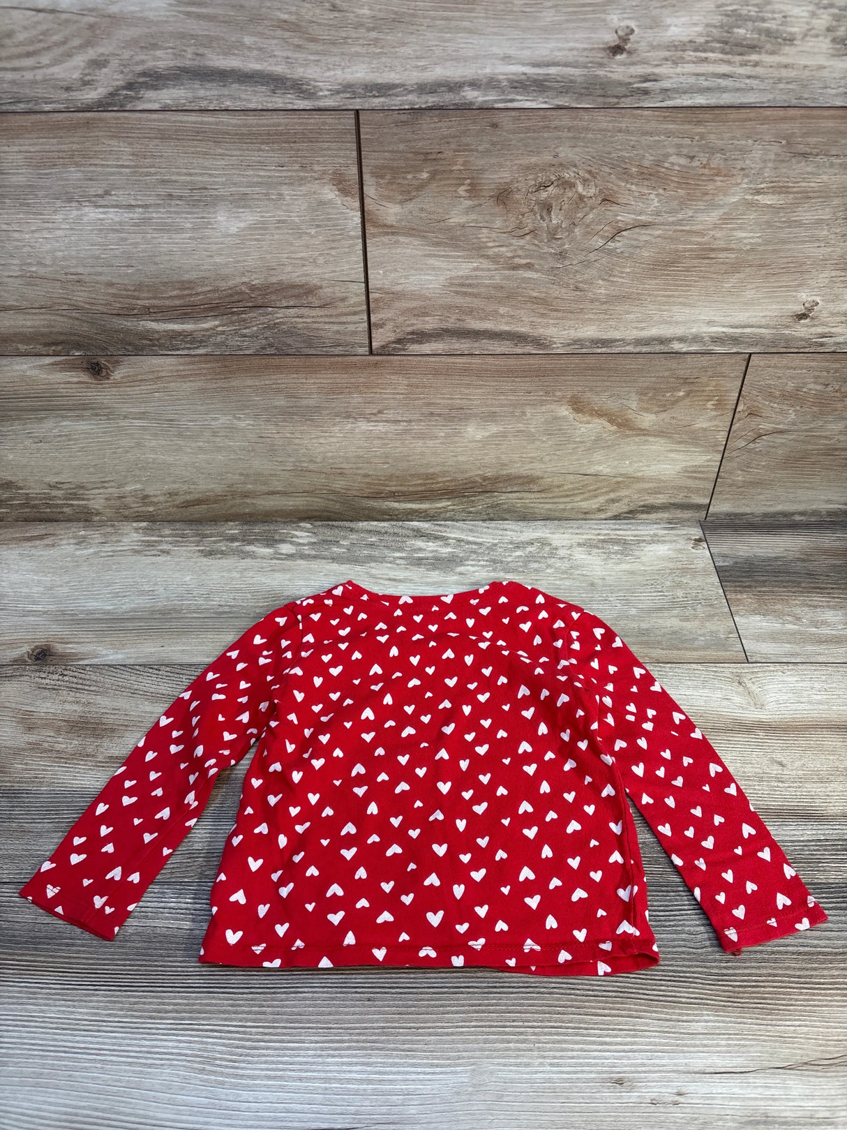 Red long sleeve toddler shirt with white heart pattern on wood background