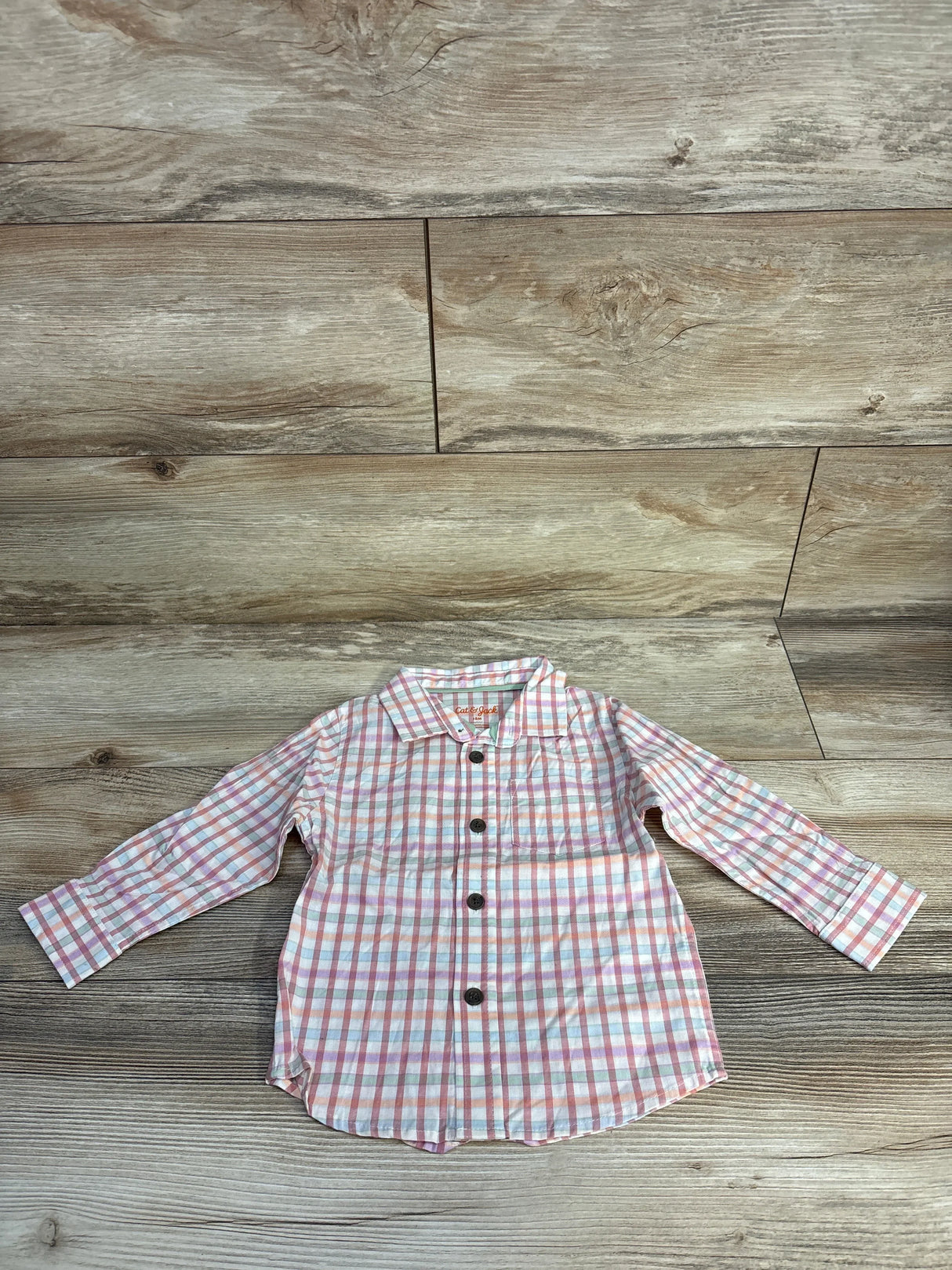 Pink and blue plaid button-up toddler shirt on wooden floor background