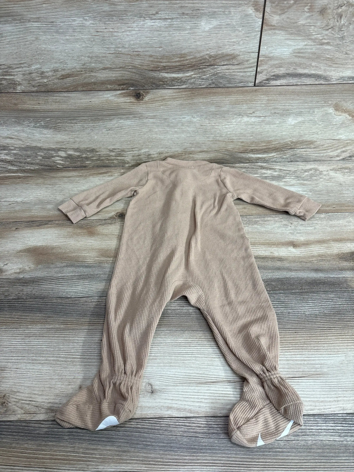 Back view of tan Nike waffle knit footed sleeper (9M) with ribbed texture and white grip dots on feet, on light wood