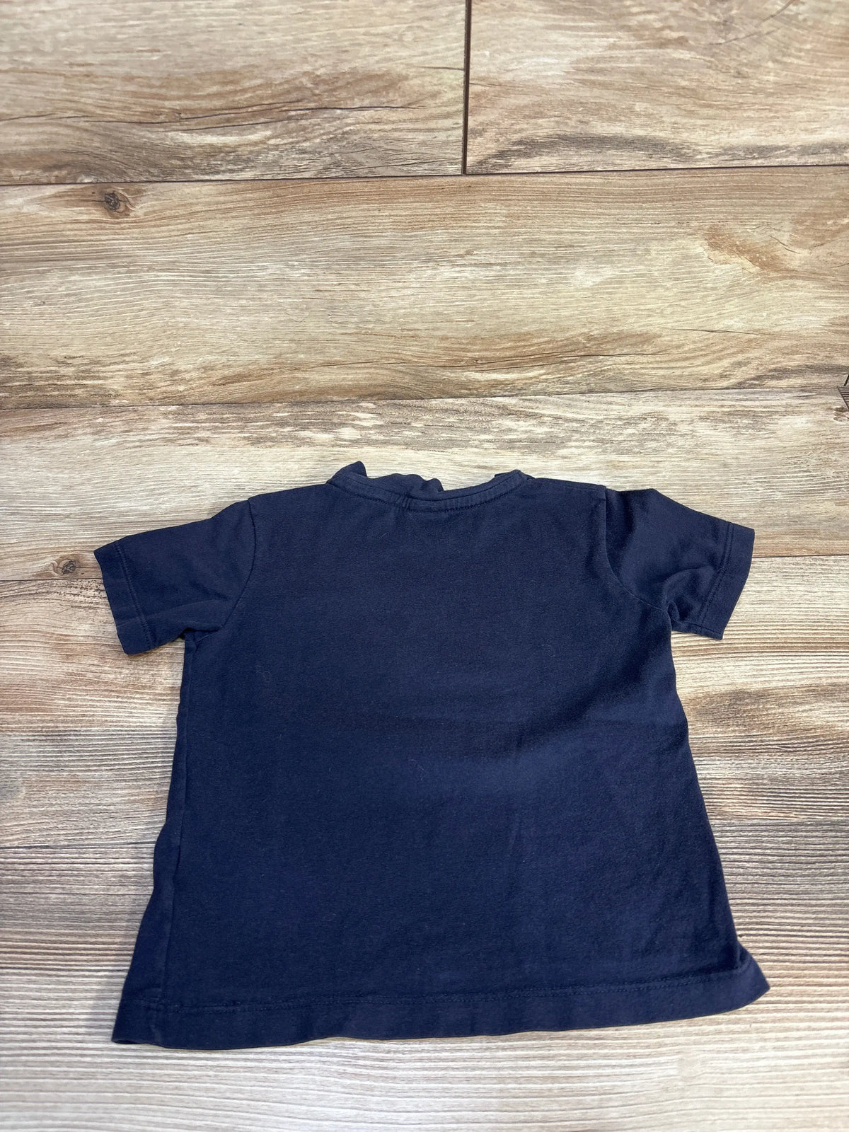 Flat view of Petit Bateau navy short sleeve shirt in size 5T showcasing plain cotton design on wood flooring
