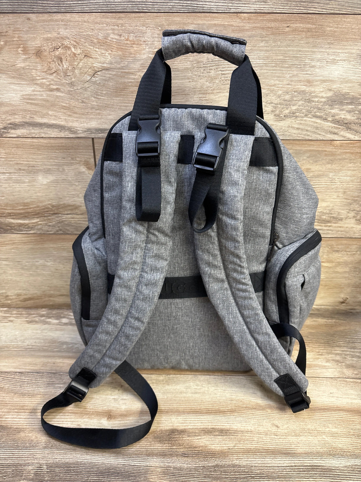 Rear view of Huggies Signature Pack diaper bag showcasing padded shoulder straps, stroller clips, and side pockets on wood background