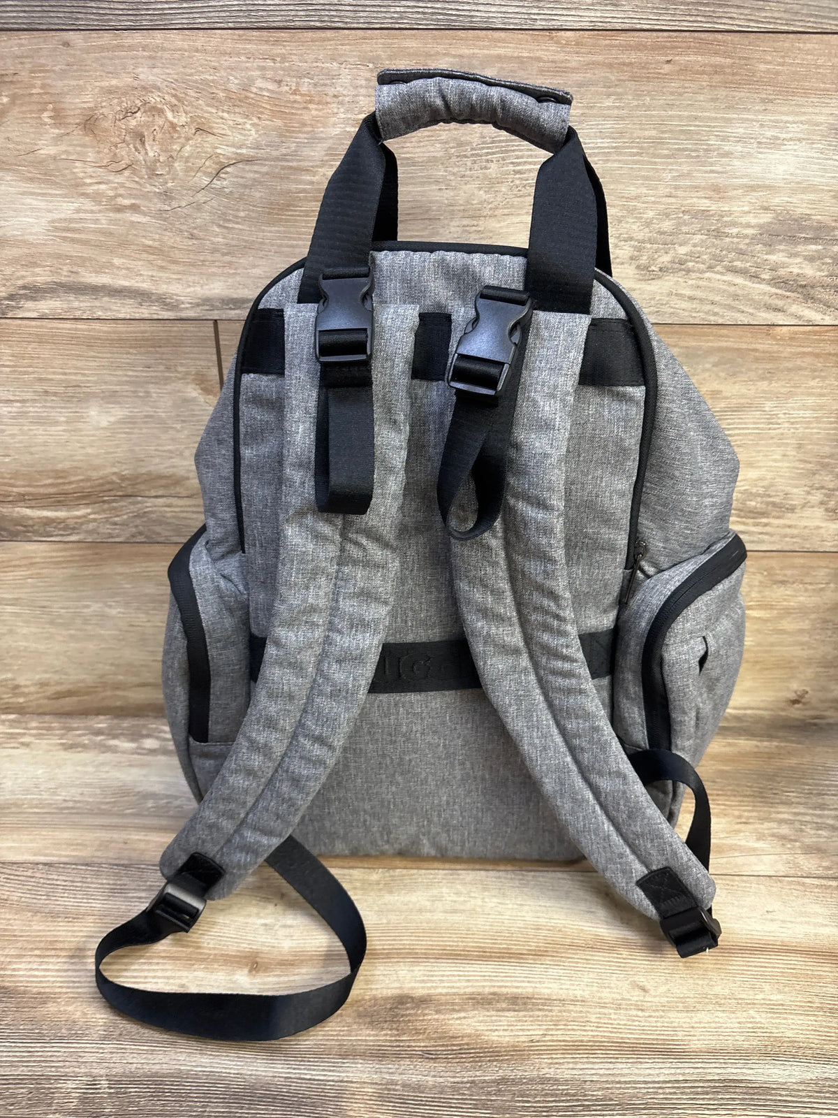 Rear view of Huggies Signature Pack diaper bag showcasing padded shoulder straps, stroller clips, and side pockets on wood background