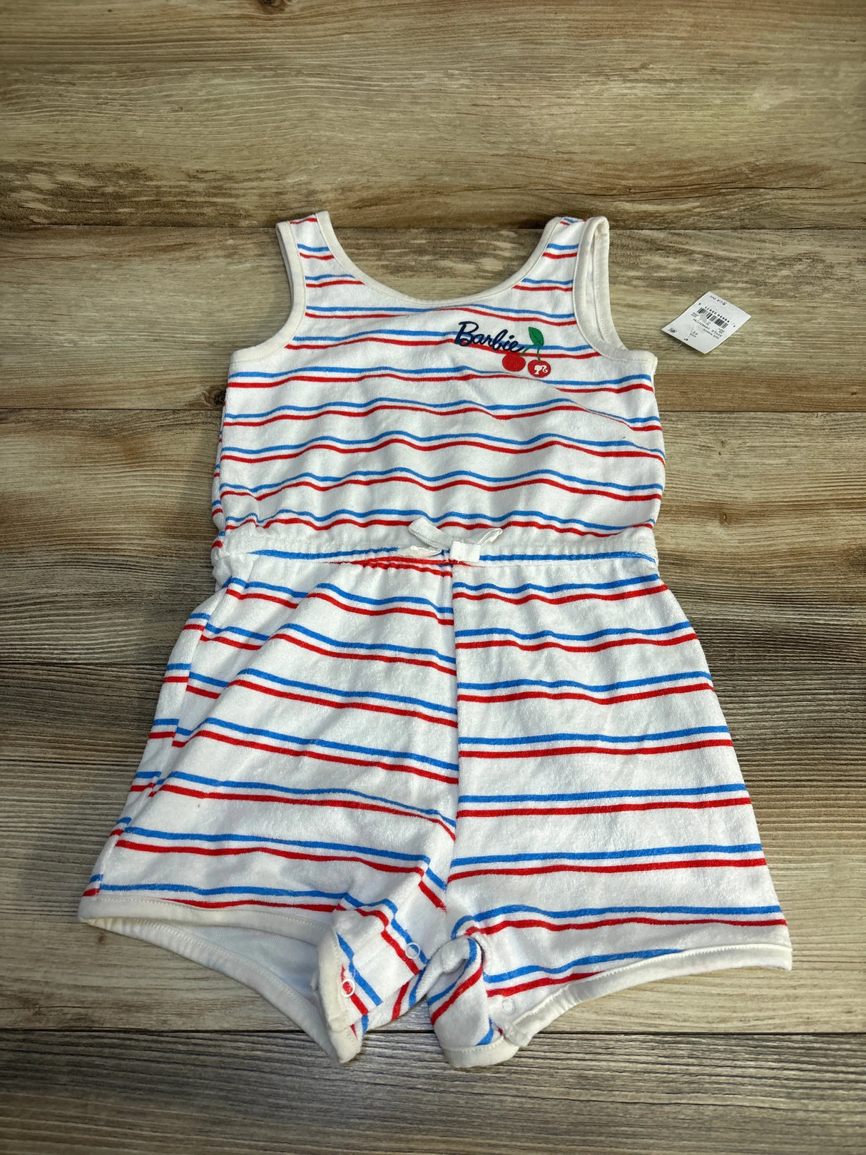 White toddler romper with red and blue stripes, cherry graphic, Barbie logo, wood background