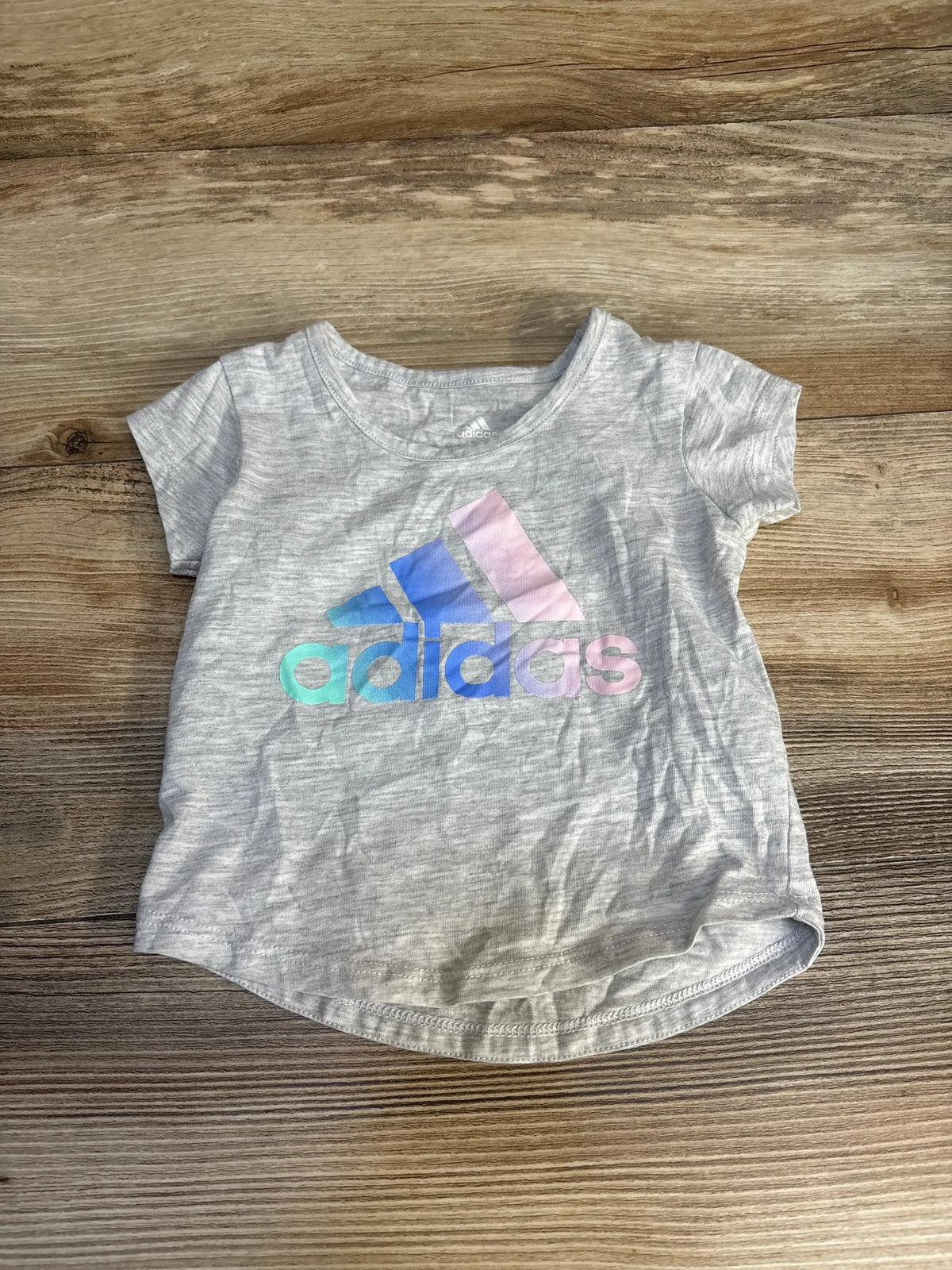 Light gray short sleeve Adidas kids t-shirt with pastel rainbow logo on wooden background