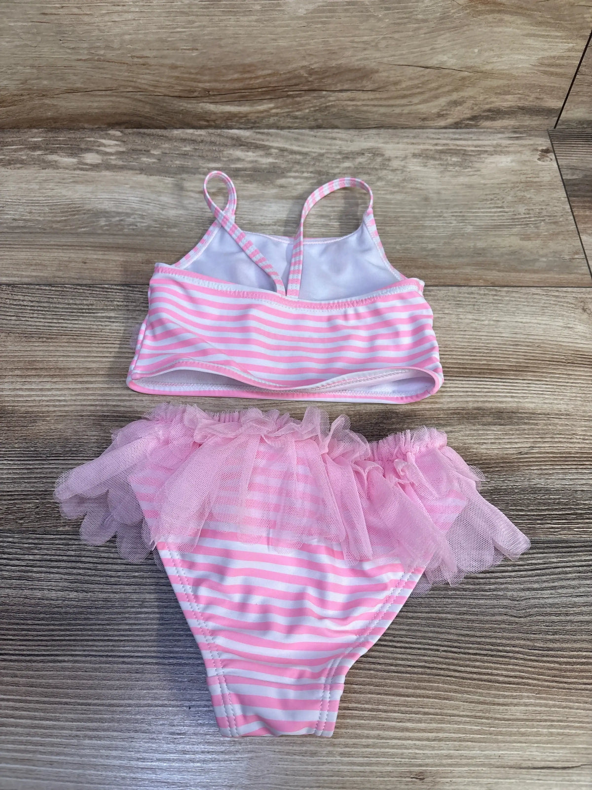 Flat lay of girls two piece pink and white striped swimsuit showcasing tulle ruffle skirt and spaghetti straps on wood background